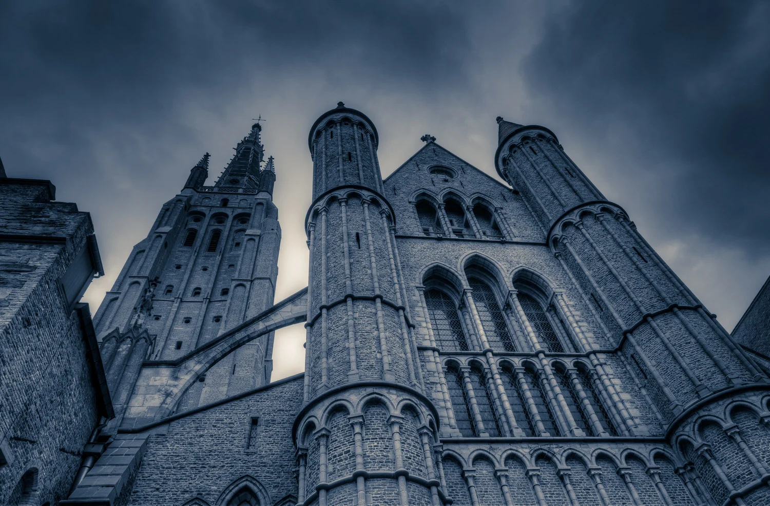 A dramatic exterior view of the Church Of Our Lady in Bruges, Belgium . This version of the image features a heavy bluish tint , which I've added for mood.