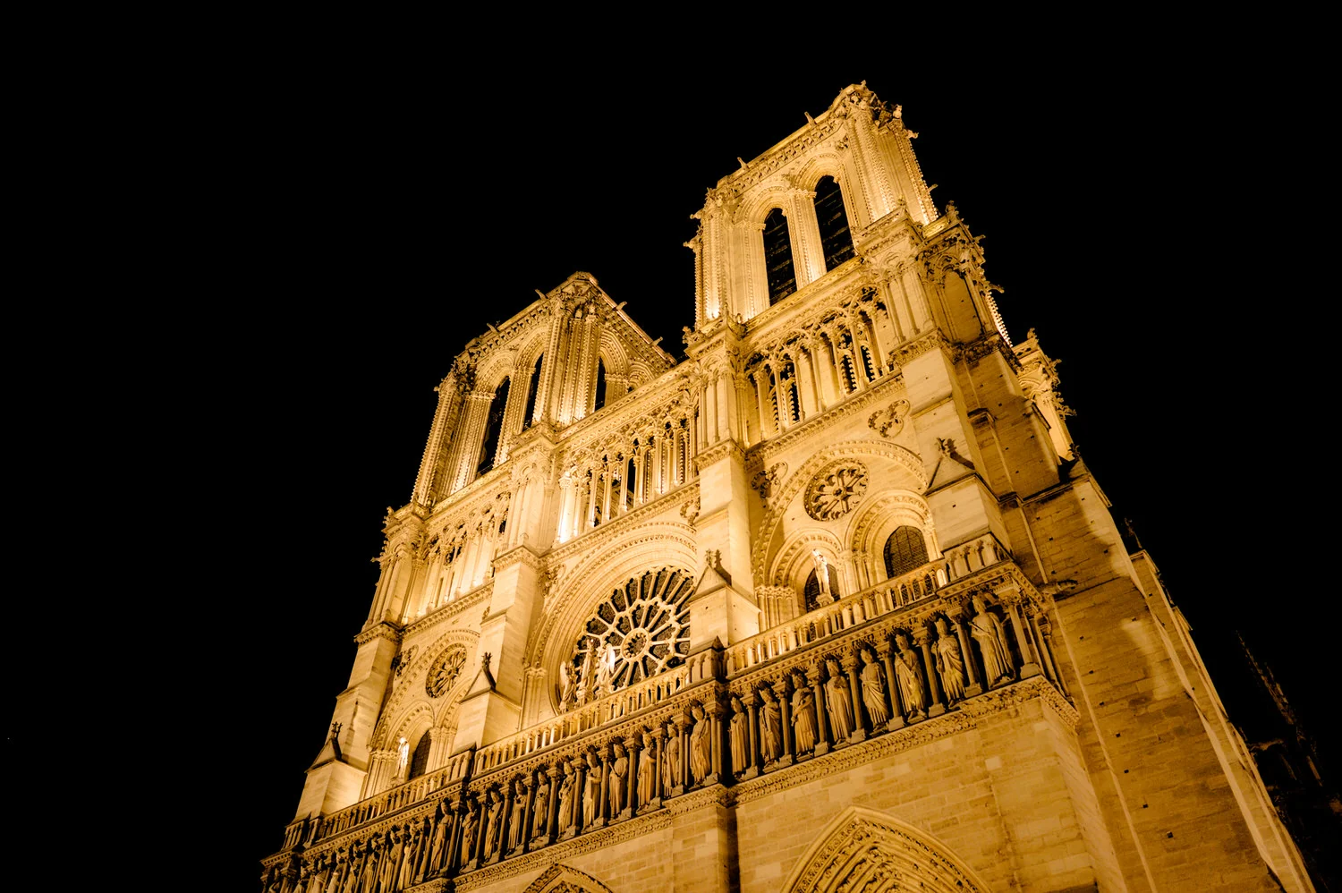 The facade of the magnificent Notre Dame Cathedral , bathed in warm light, in Paris at night .
