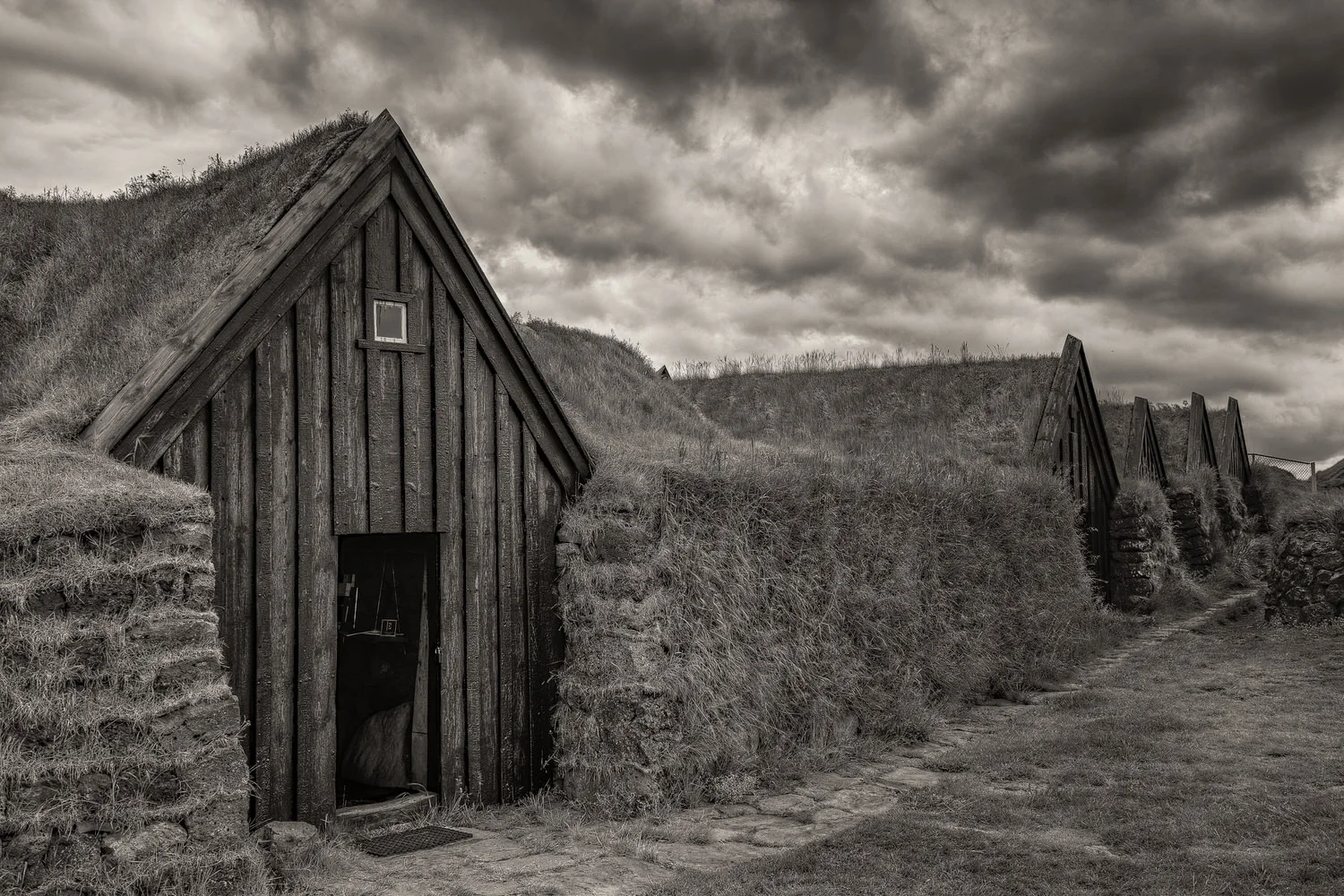 A series of well preserved, grass topped traditional farm buildings in southern Iceland . The light was silver grey and the approaching storm helped abstract the scene from the now and transport it back in time.