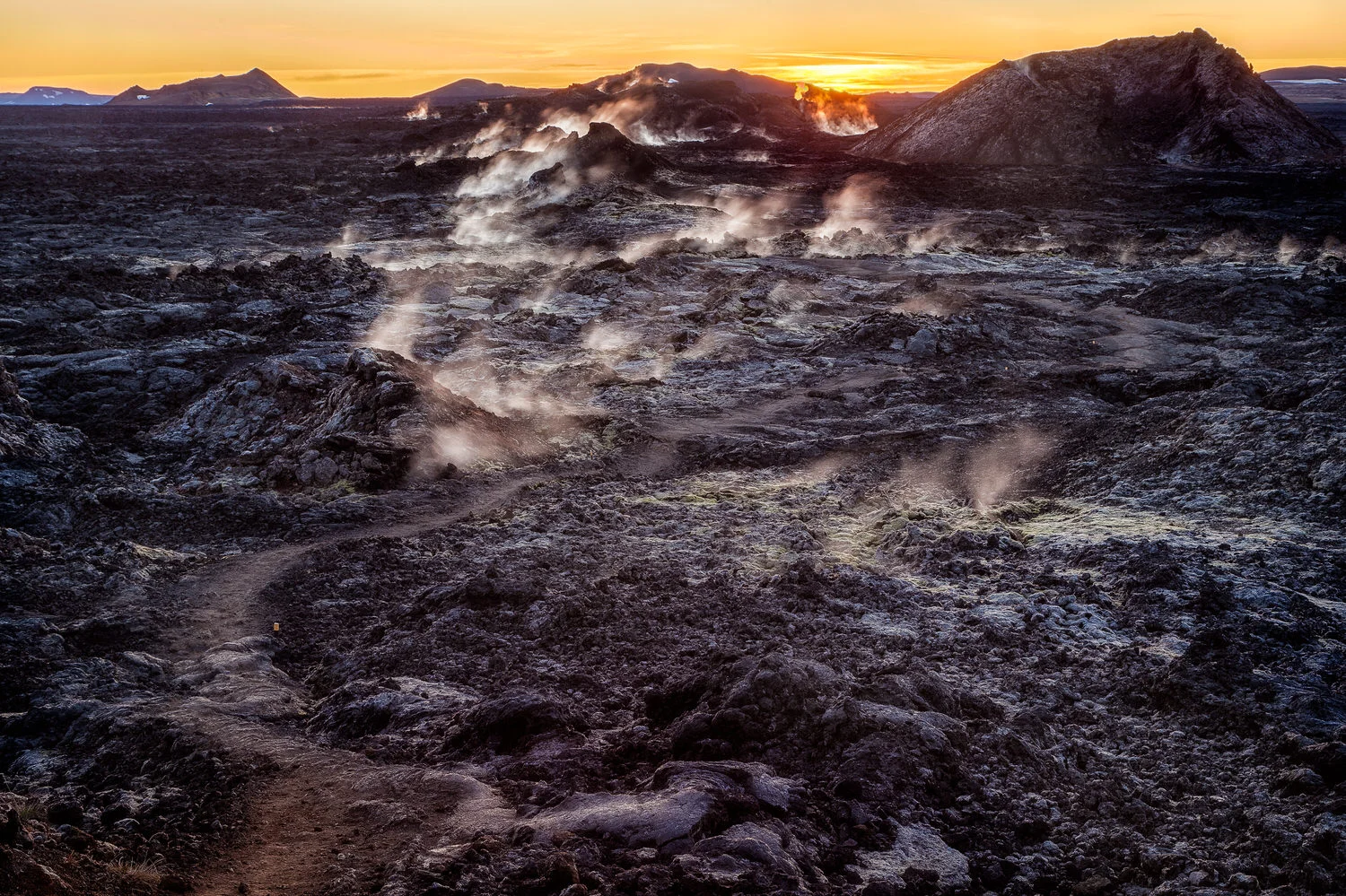 A narrow path leads through black ash, that will melt your shoes, and steaming vents in the Leirhnjukur Lava Fields near Myvatn in Northern Iceland .