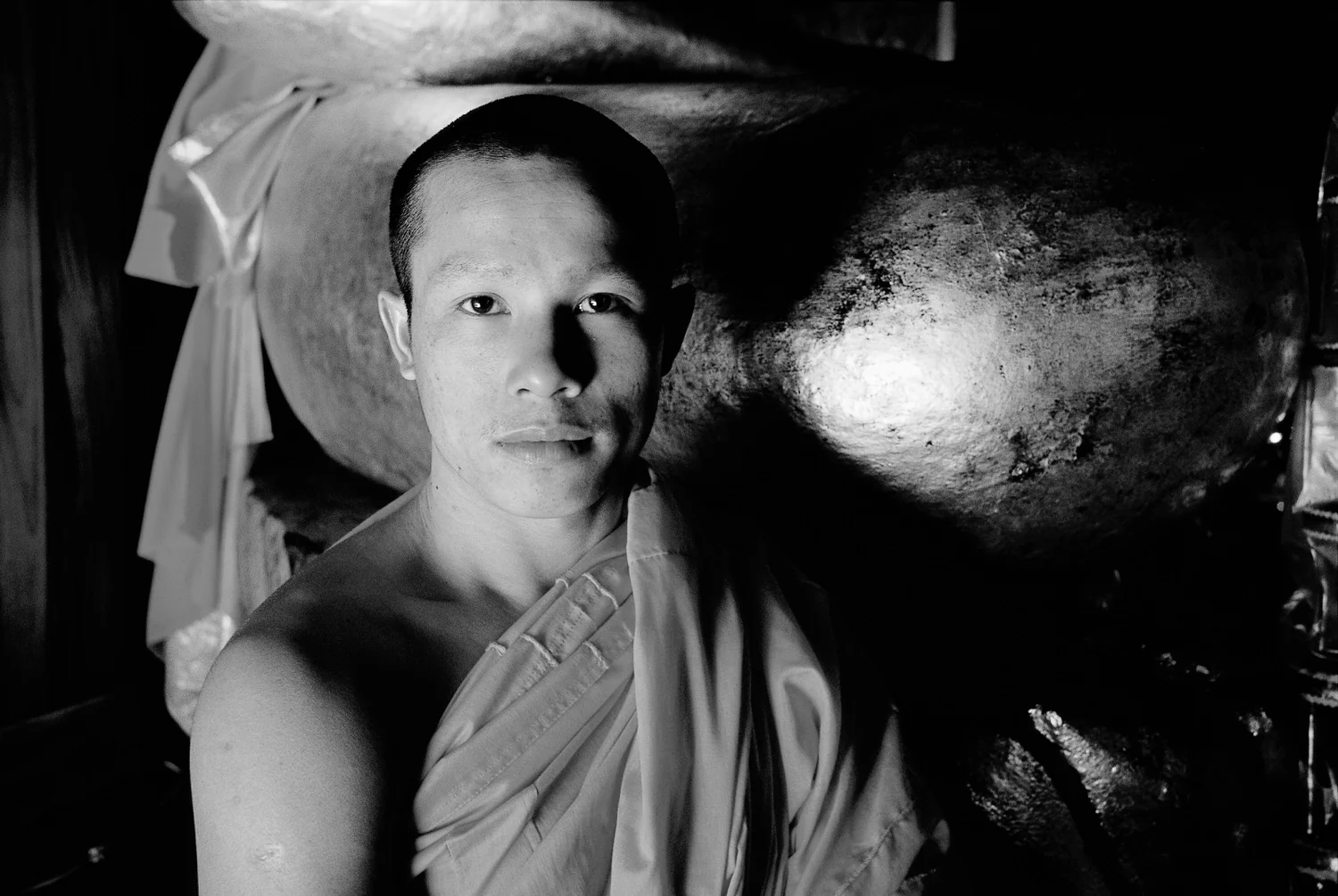 A black and white portrait of a monk , made with side light, in a Buddhist temple in Luang Prabang, Laos .