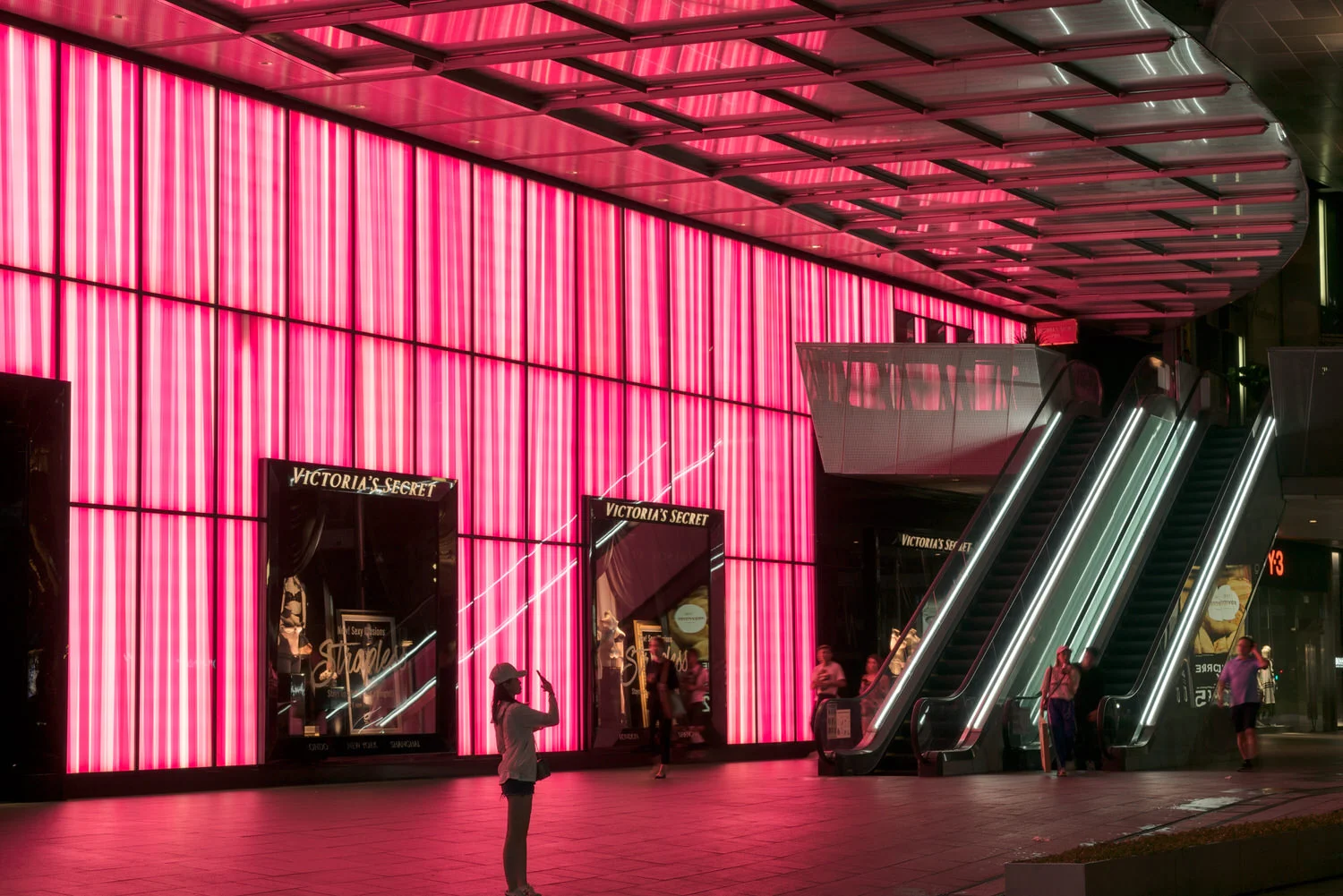 Vibrant pink light provides wonderful backlighting for this street scene along the famous Orchard Road in Singapore .
