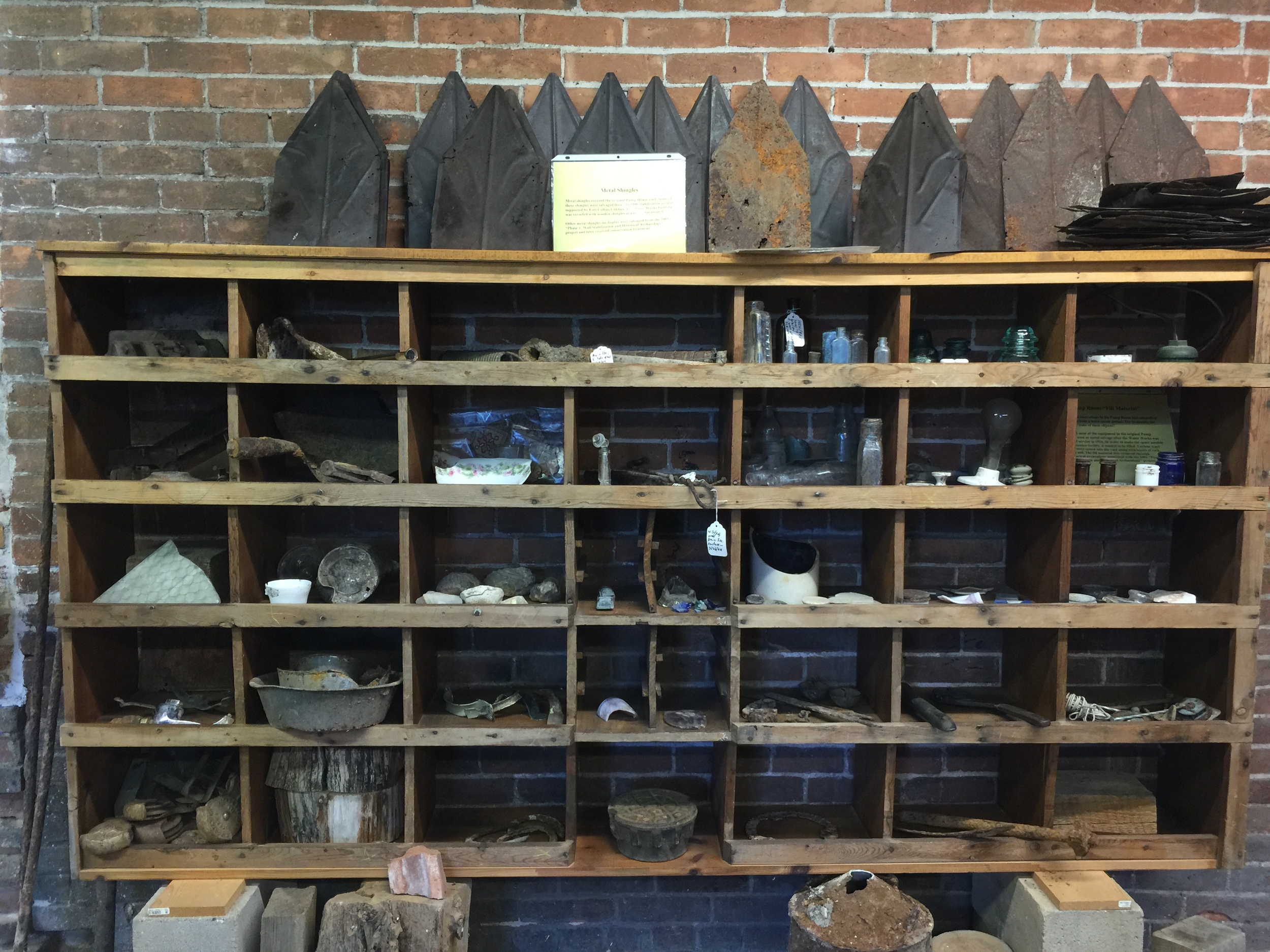  Some original metal shingles were salvaged and restored and are displayed on top of these shelves. The shelves also contain other artifacts recovered from the site during restoration/conservation efforts. 