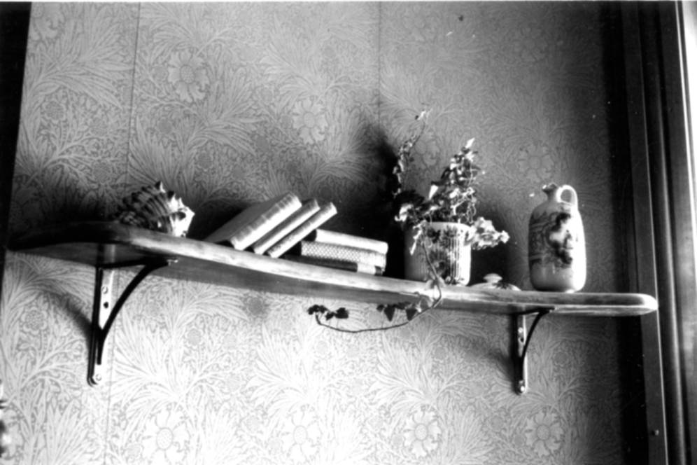 Circa 1980. Black and white photograph of the interior of the Avery House located at 328 West Mountain Avenue; Fort Collins, Colorado.This photo shows a small book shelf/ledge with a few books and a few decorations on it. 