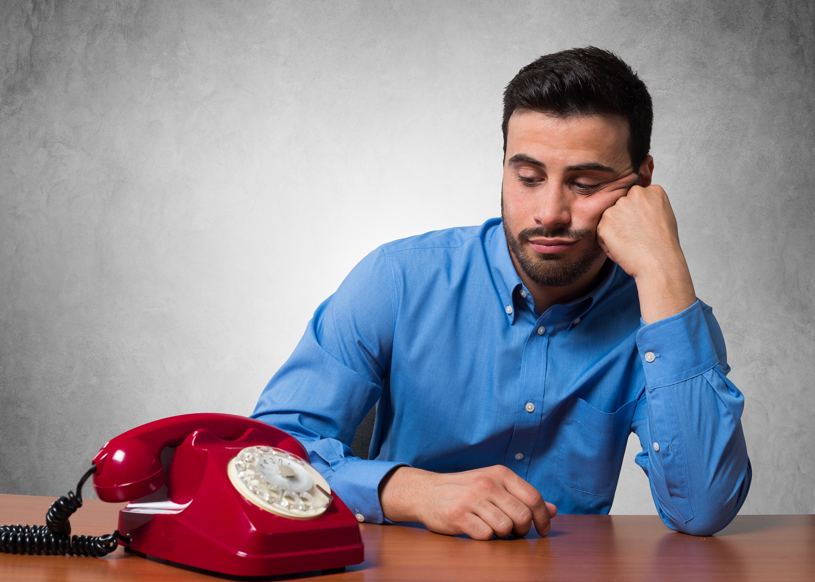 Man waiting for a call to come through on an old, red, rotary phone.