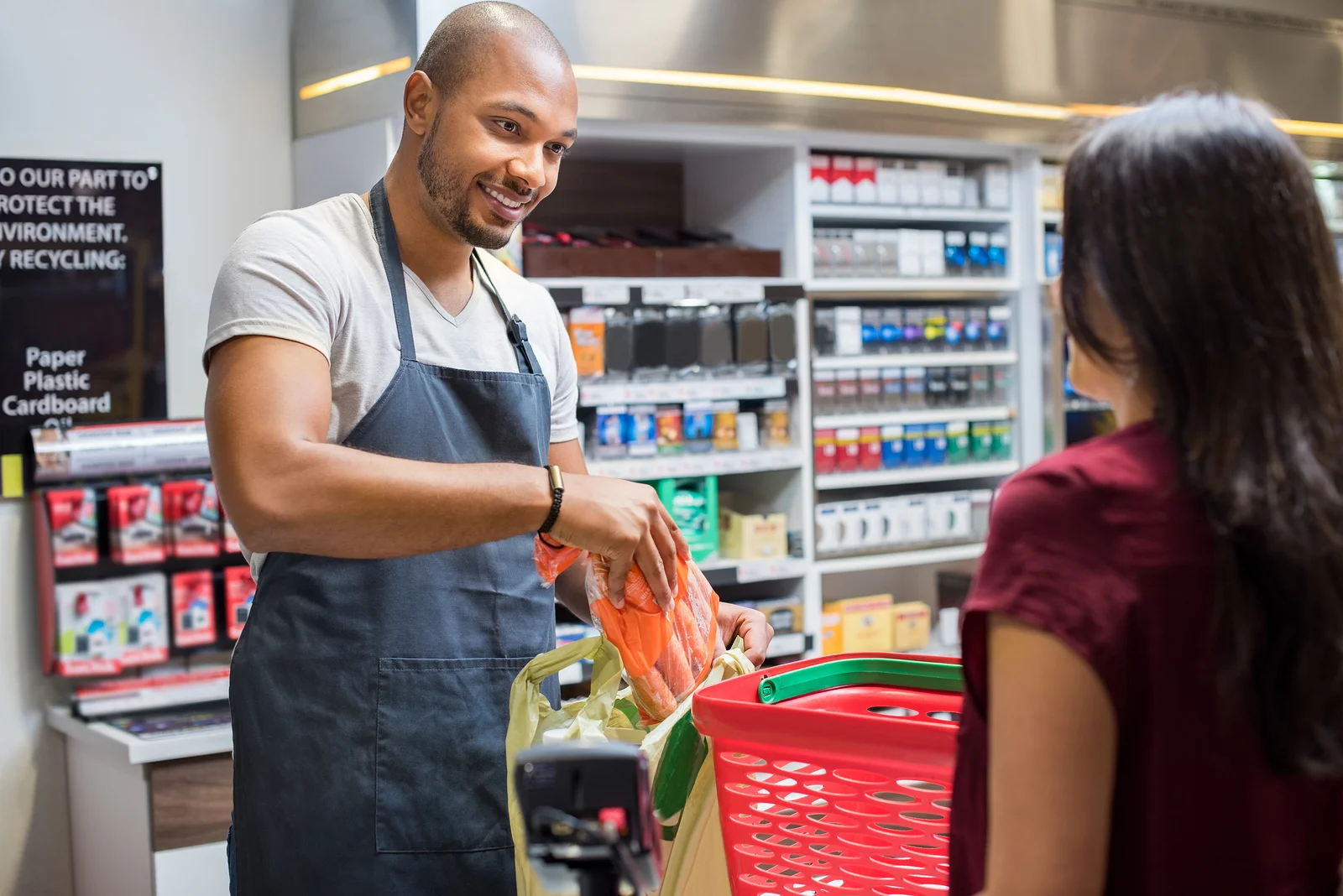 A smiling grocery store cashier bagging groceries for a customer.