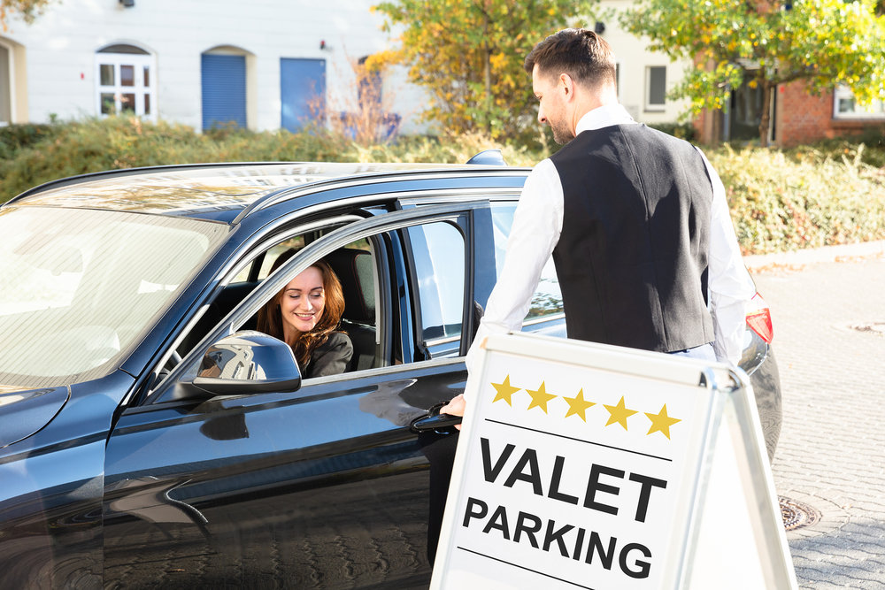 A valet parking attendant is opening the car door for a guest.