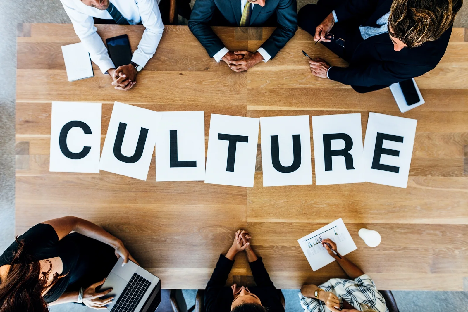 A group of colleagues sitting at a conference table with the word “culture” written on it.