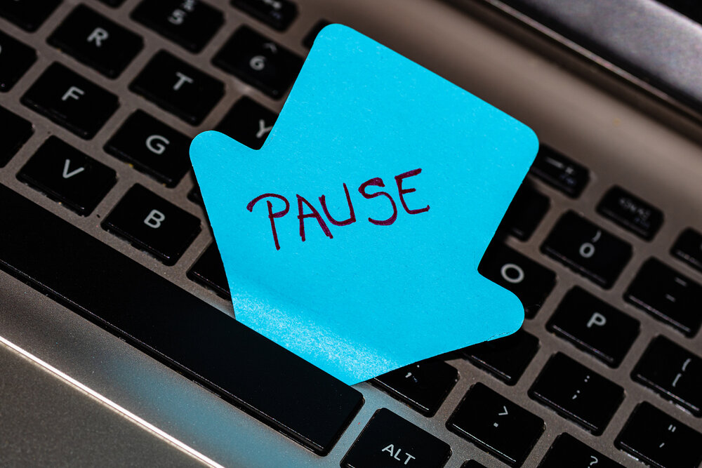 A giant sticky note on a computer keyboard with the word “pause” written on it.