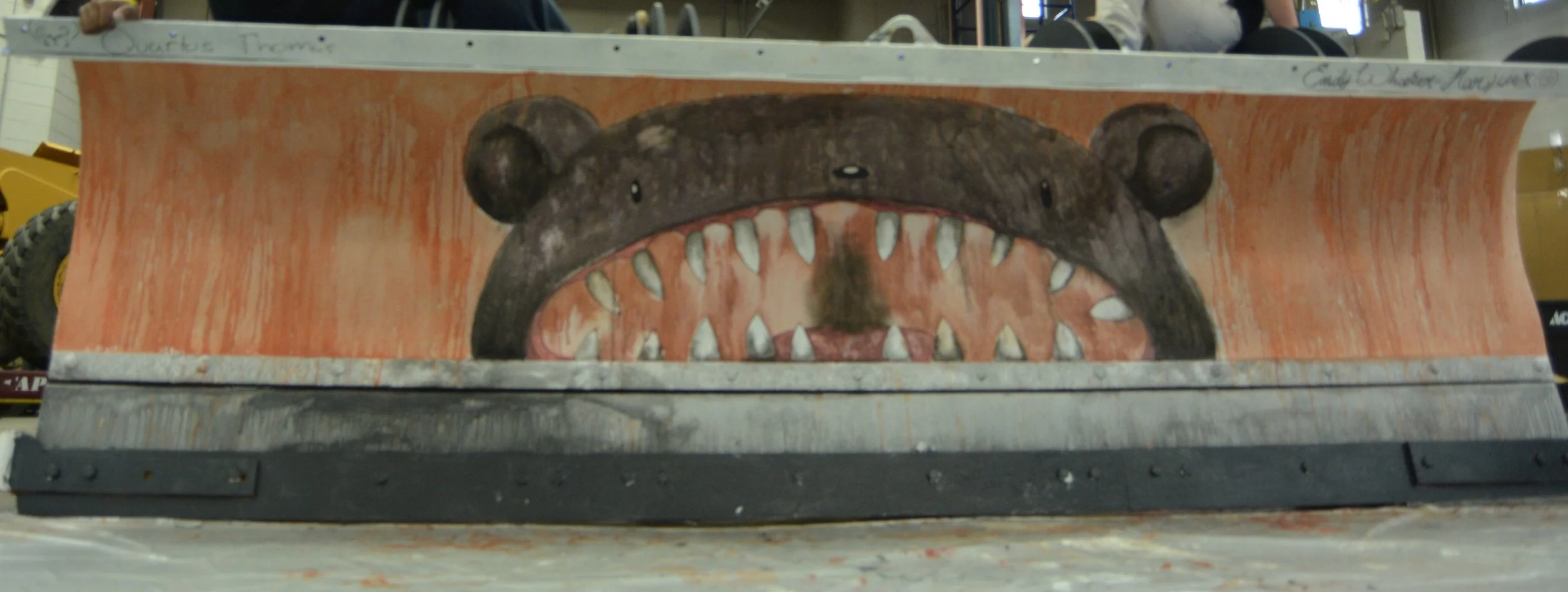 Painting of a bear's face with open mouth and sharp teeth on a wooden surface.