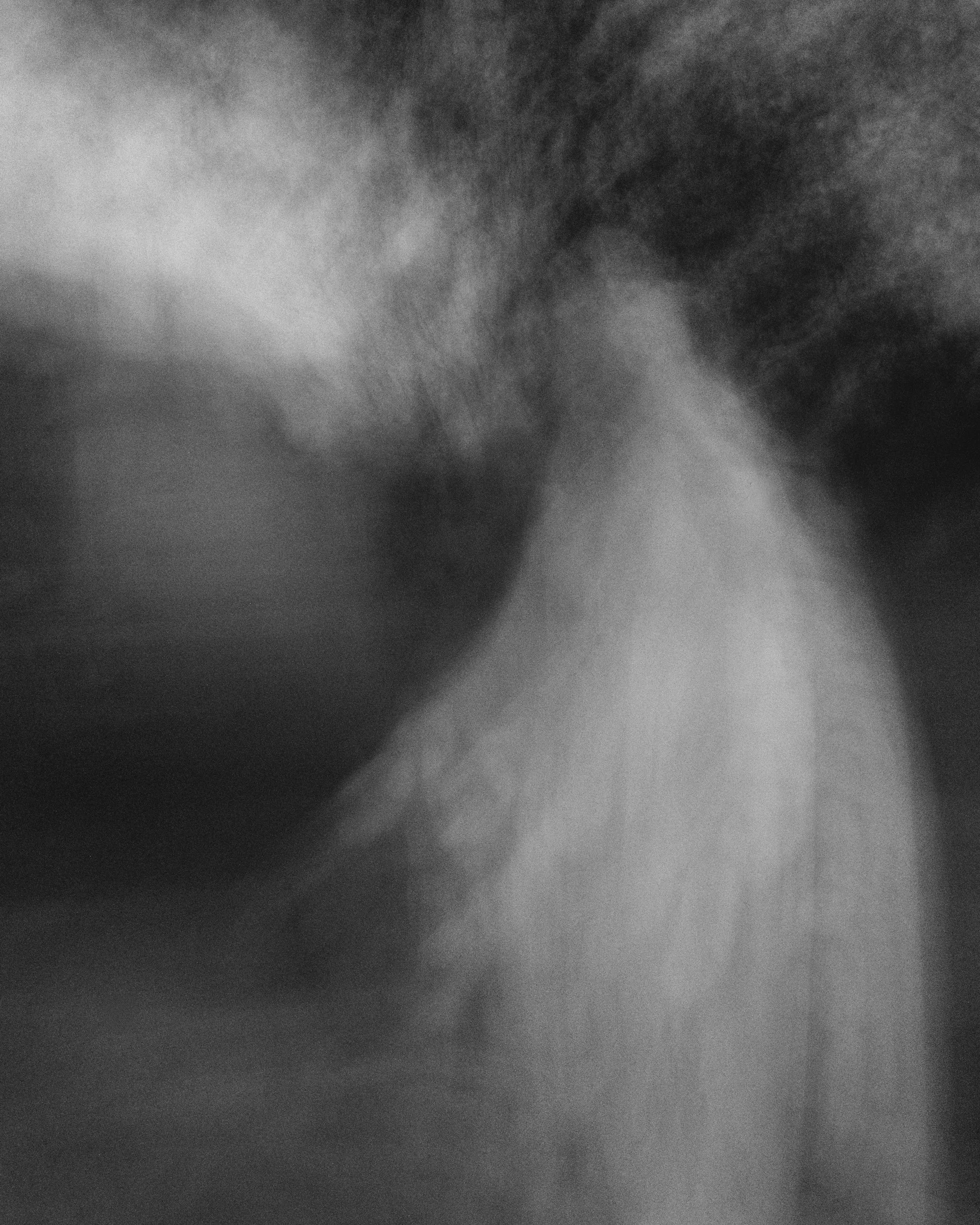 A close-up black and white image of a person's hand holding an object, with a dark, blurry background.