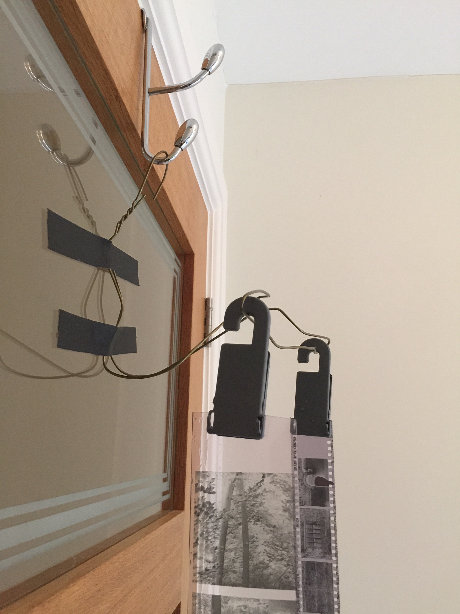 Film drying in the darkroom. My drying rig is expertly crafted from a metal clothes hangar, gaffers tape, film hanging clips and a over-the-door hook. 