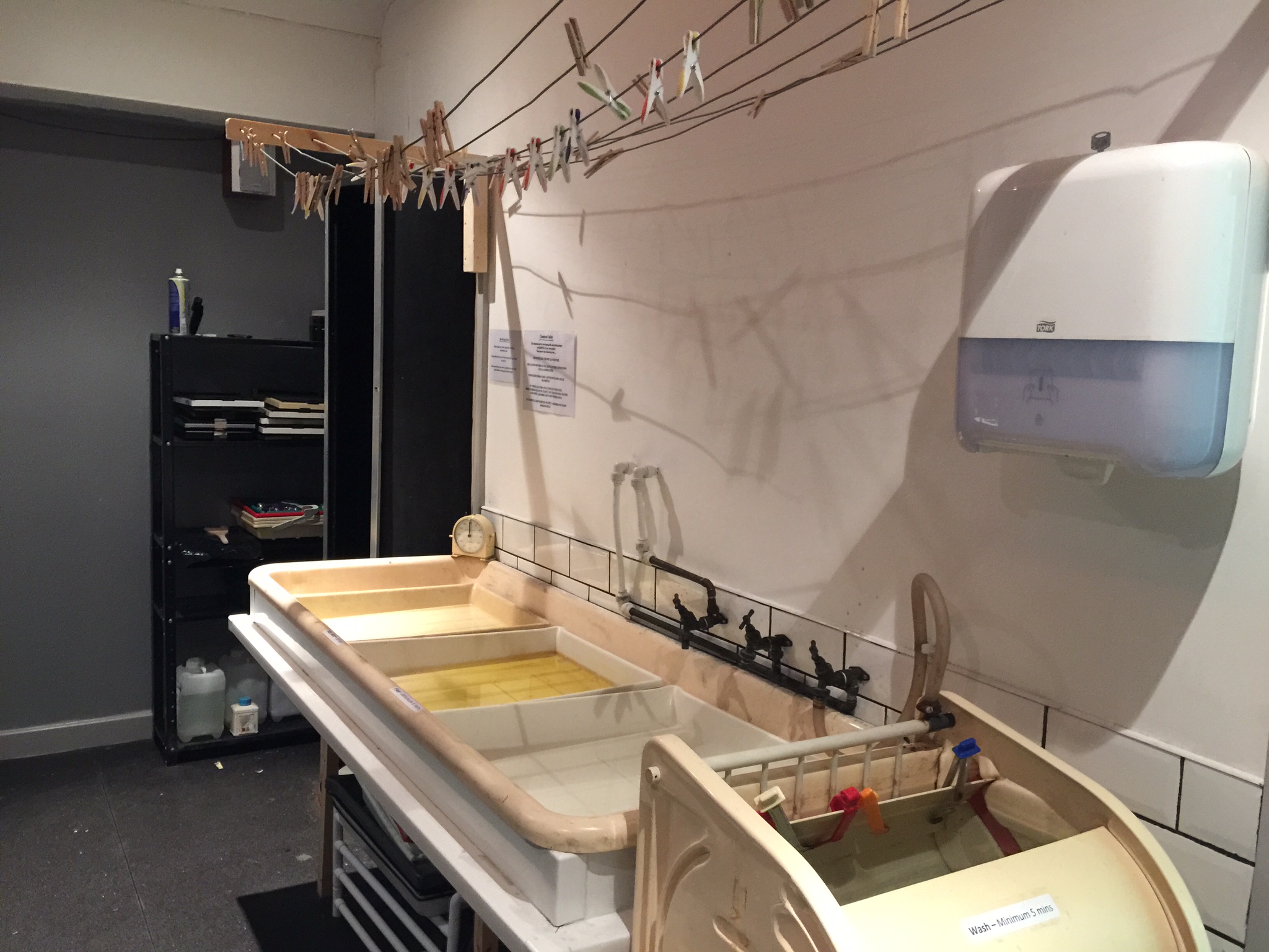 The wet side of the darkroom. Each tray holds a different developing chemical. The black and silver thing at the end is the light tight door.