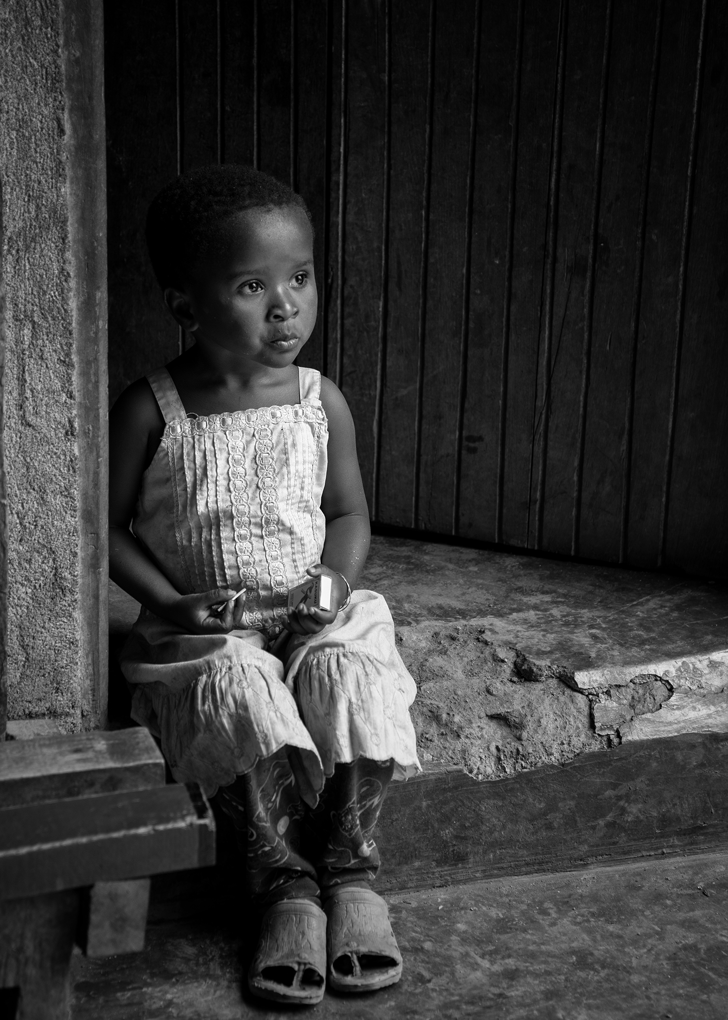 The daughter of a coffee farmer sits on the mud step outside her hut