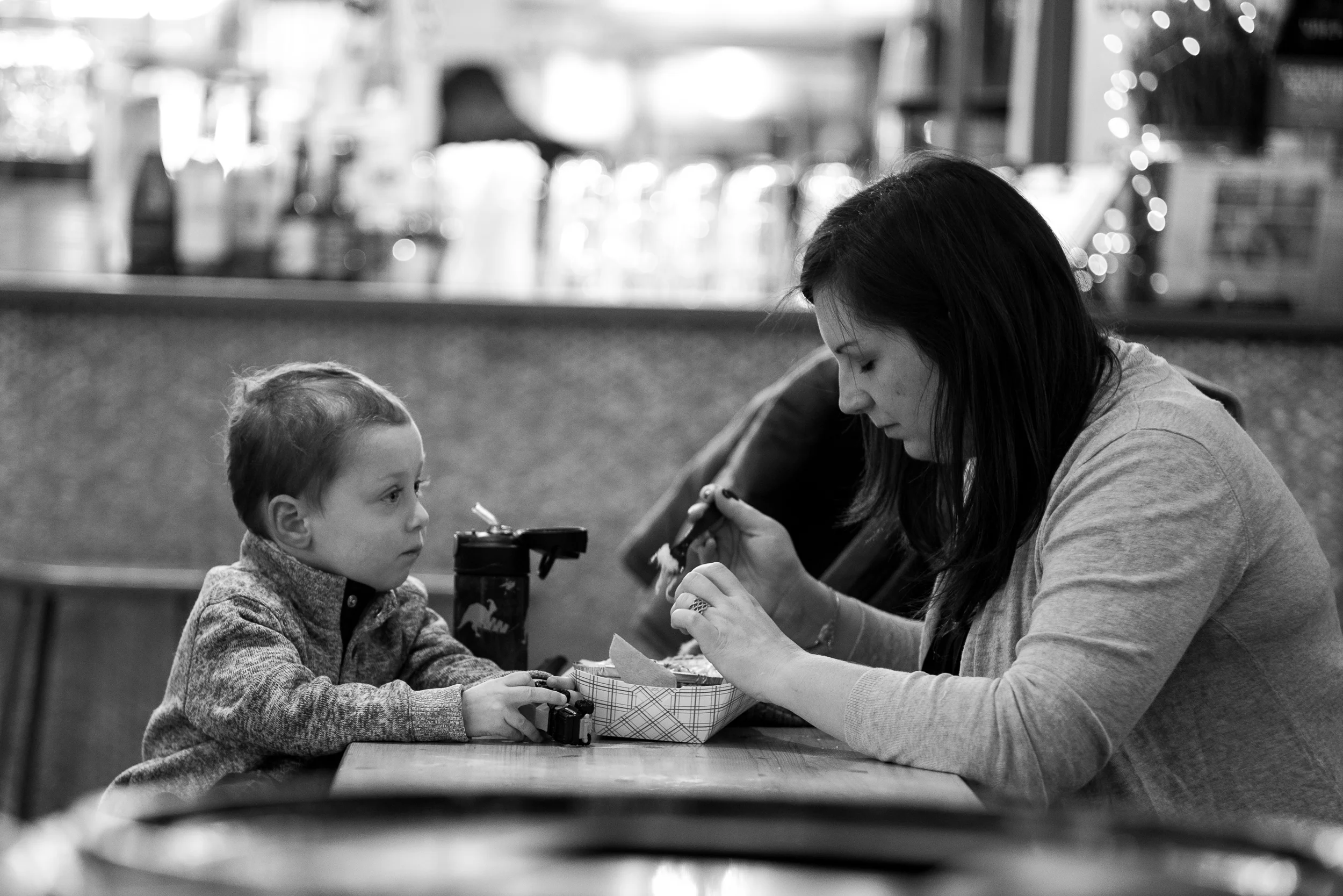Sharing a Snack. A mom and son enjoy a Sunday morning snack at an indoor food hall in New York. The scene is very busy with elements that could distract from the story of the shared meal, but selective focus and bokeh help me isolate them and tell the story the way I want. Leica M10 with 90mm Summicron f/2.