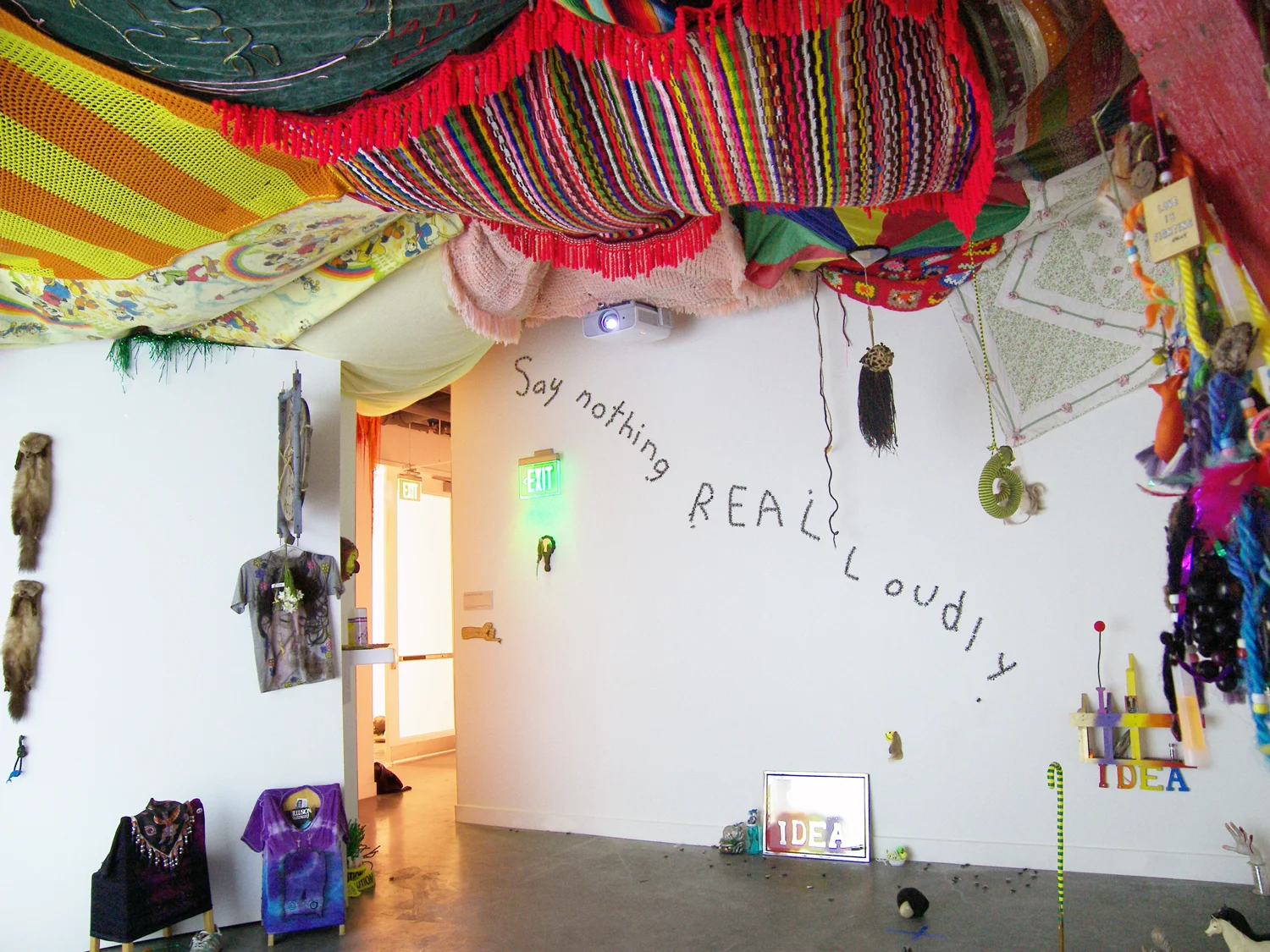 Say Nothing Real Loudly Installation with performance 2009 Installation consists of various kinds of sculpture, video projection, audio loop (“That’s What You Get For Loving Me”by Peter, Paul and Mary), found tchotchkes, stolen tchotchkes, painted wood, plastic flies, mirrors, stickers, afghans,posters, braids, glow sticks, yarn, desiccated bats, t-shirts and tape.