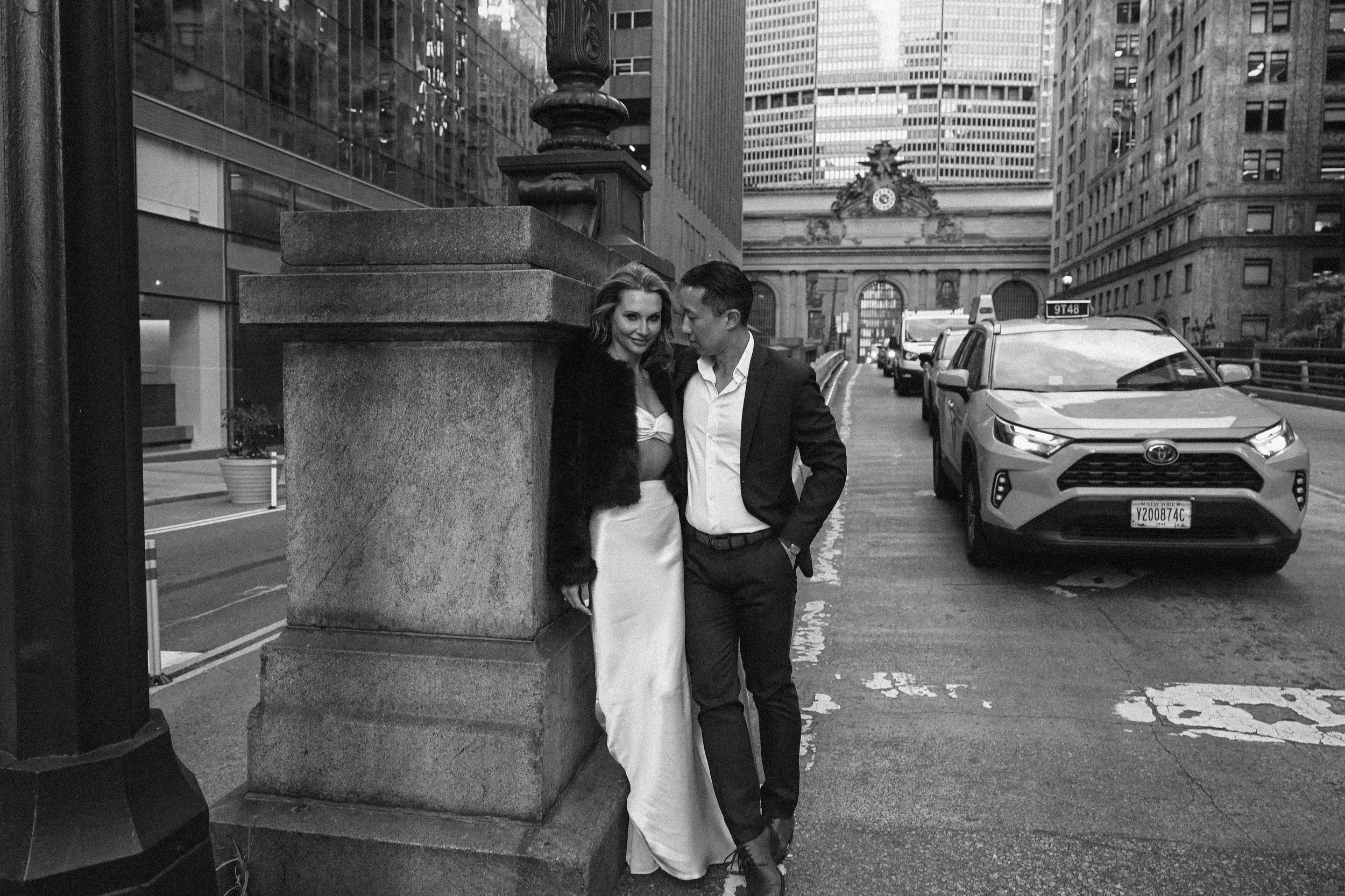 Black and white engagement photos near Grand Central Station in Manhattan, featuring a couple embracing on a classic NYC street, photographed by NYC wedding photographer Robert Carlo.