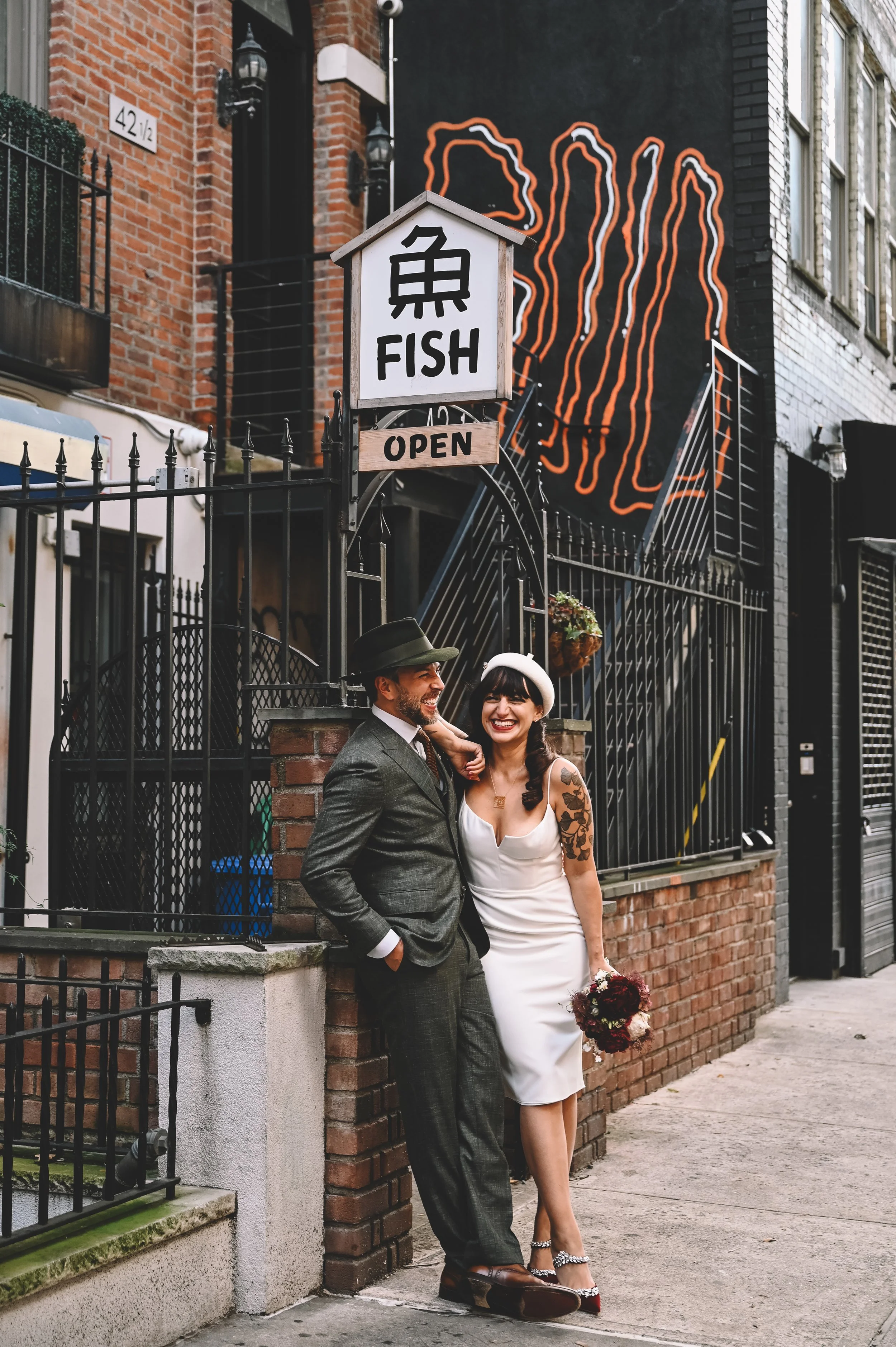 A smiling couple in vintage clothing standing outside a fish restaurant on a city sidewalk.