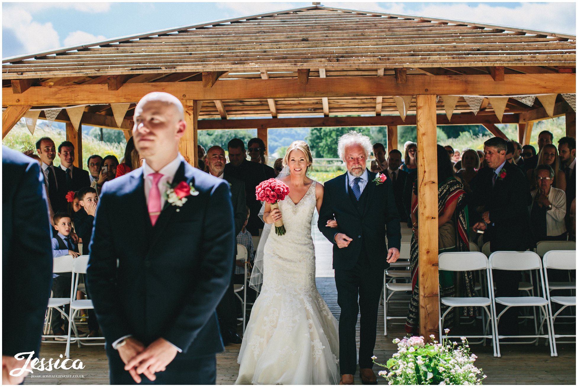 the bride walks down the pathway to her groom who is waiting under the bridge