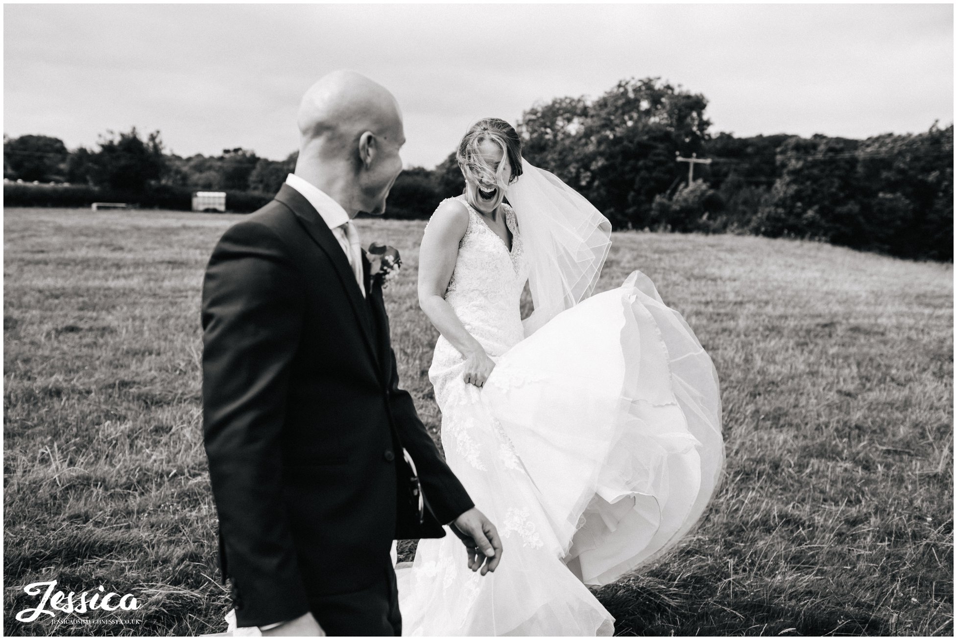 windswept bride walking through fields with her groom - tower hill barns wedding photographer