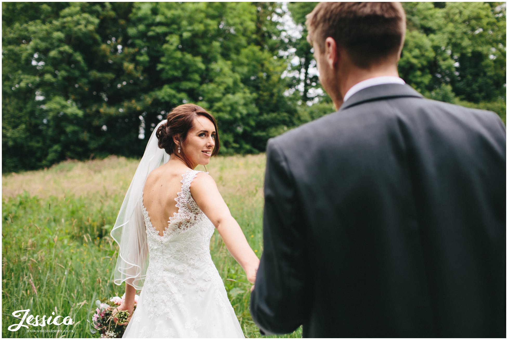 bride & groom walk through meadow on their wedding day at Three Hills Barn, Torpenhow