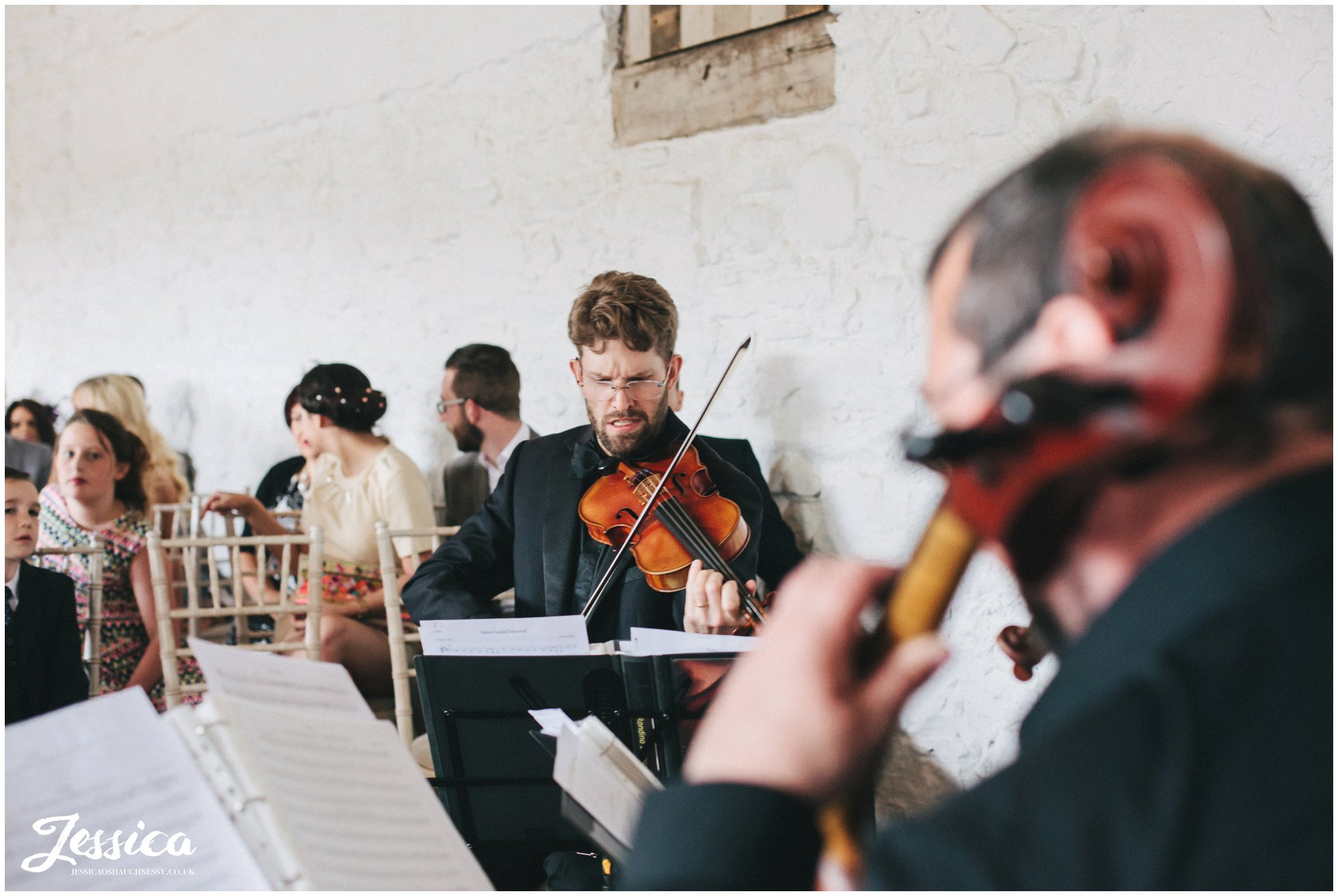 violinists play as bride walks down the aisle in bank barn, askham hall