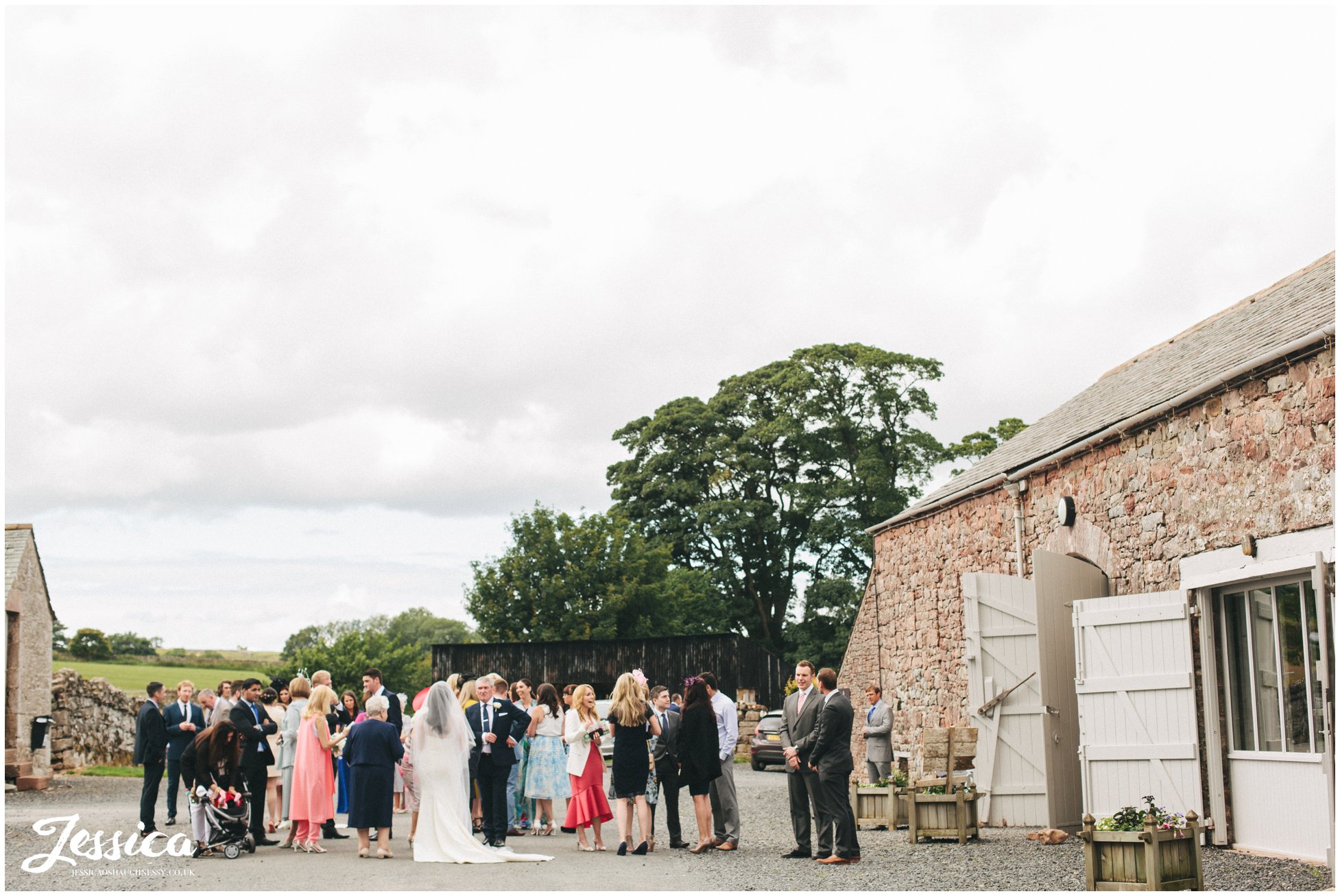 guests gather outside bank barn after the wedding at askham hall in penrith