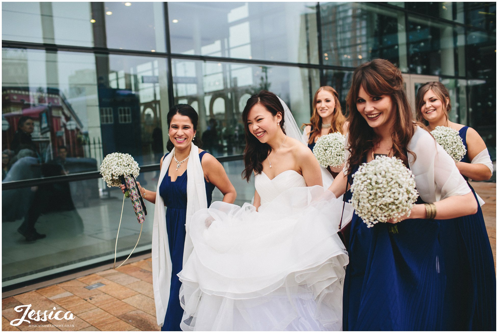 Bridesmaids carry brides dress as she walks through Media City in Manchester to her wedding at On The 7th