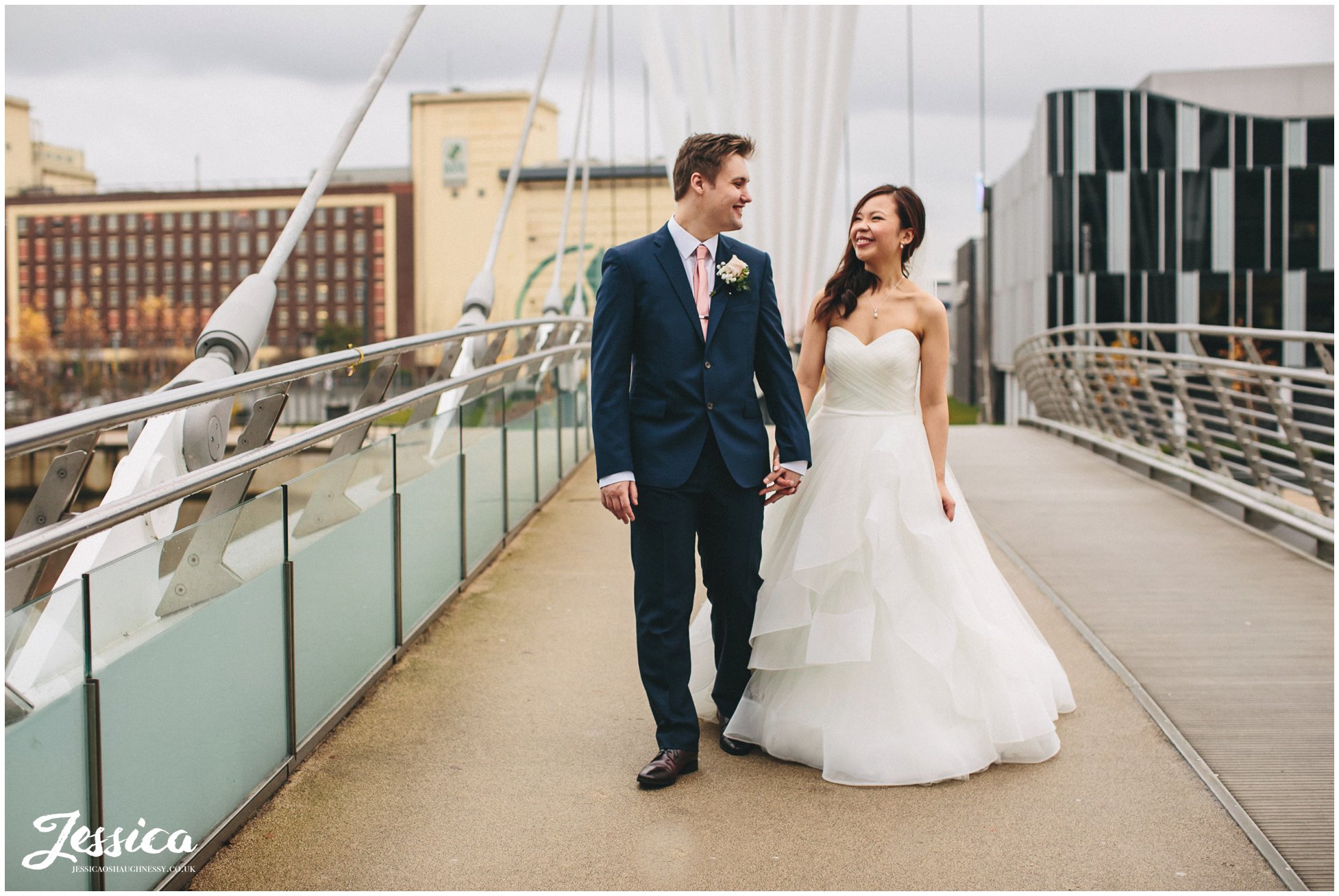 newly weds walk hand in hand over The Media City Footbridge - manchester wedding photographer