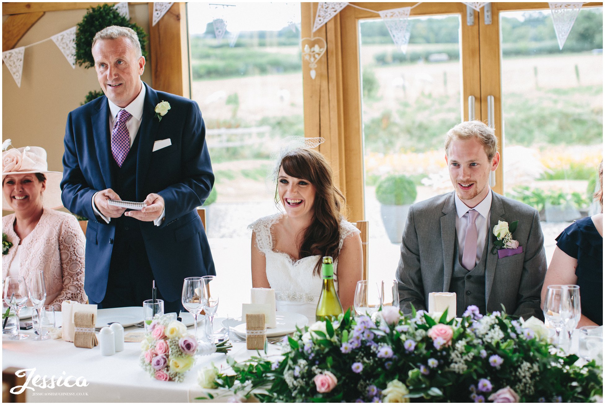 bride laughs during the father of the bride's speech in barn