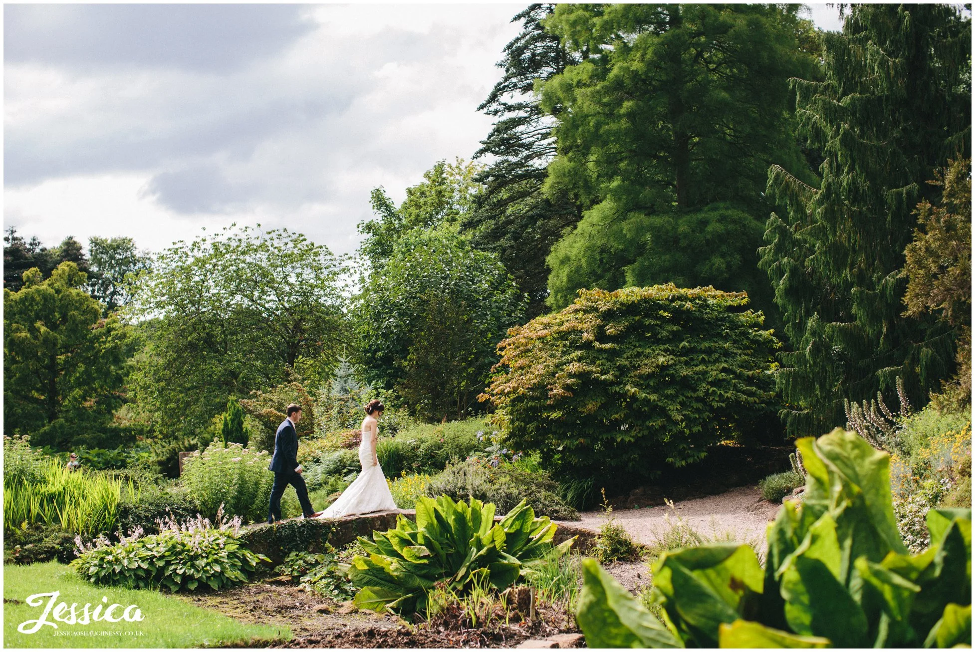 bride & groom walk over a bridge in the distance, ness gardens wedding photographer
