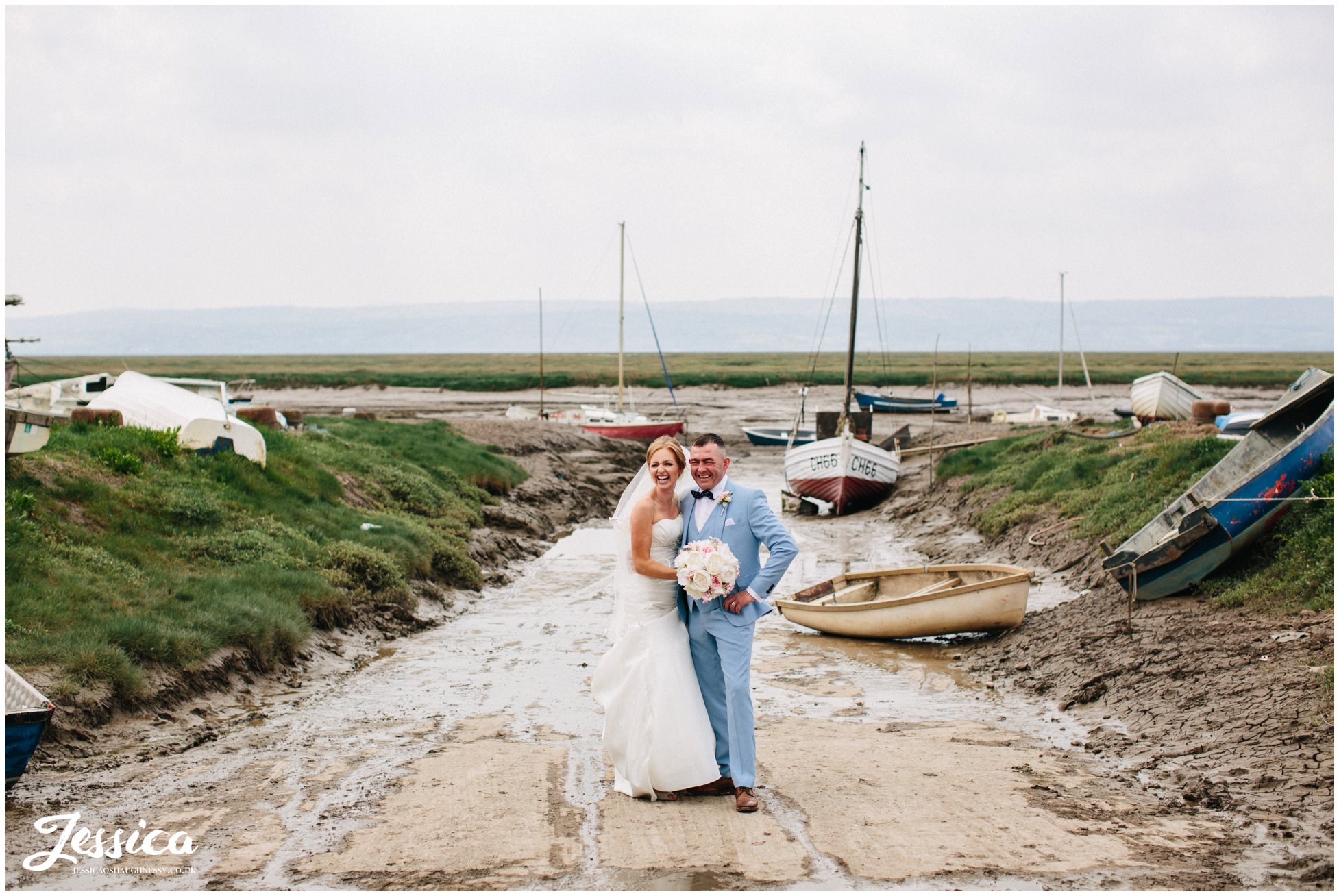 newly wed's stand between boats on the waterfront at their wedding at sheldrakes