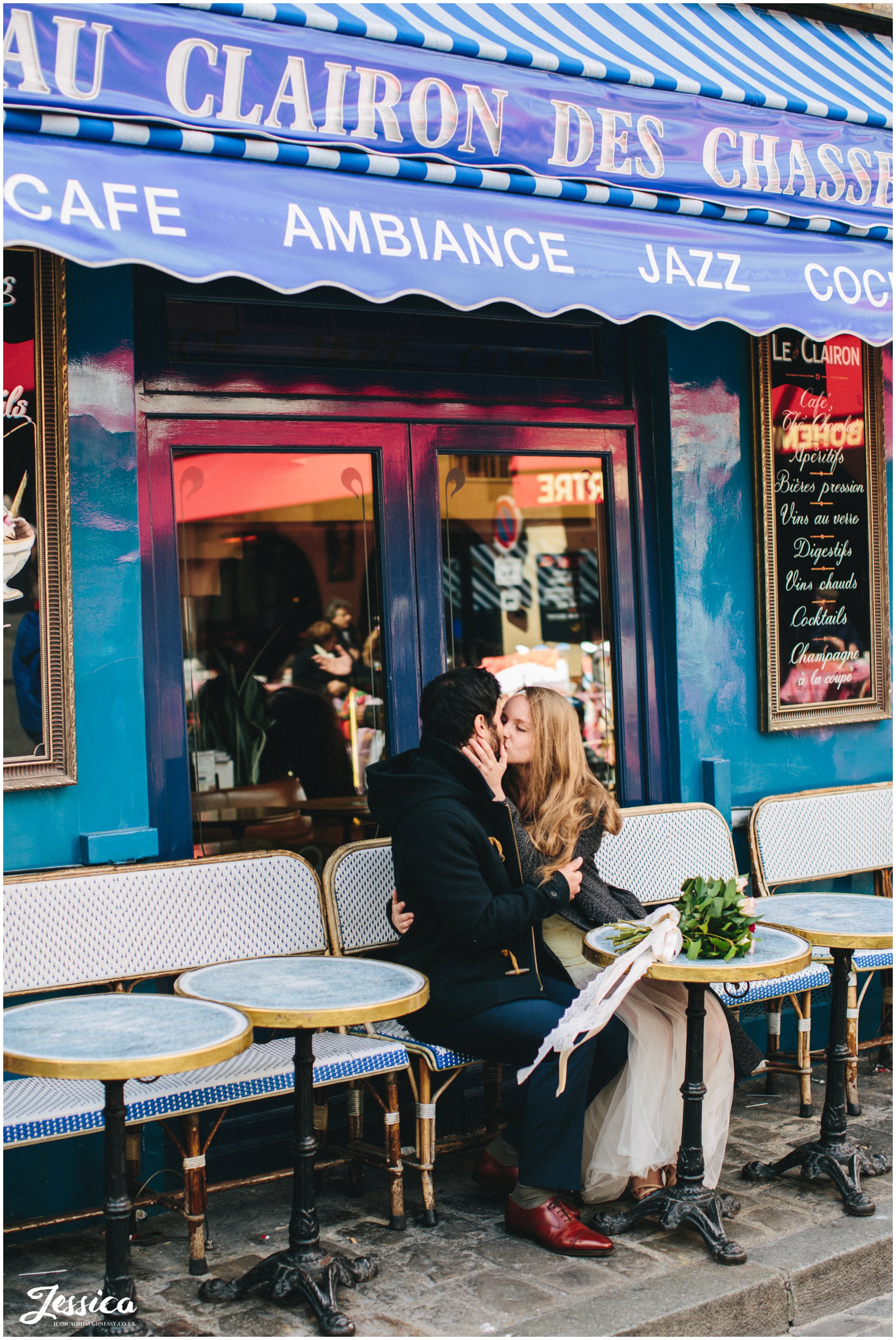 couple sit kissing in front of a blue cafe in mont marte, paris