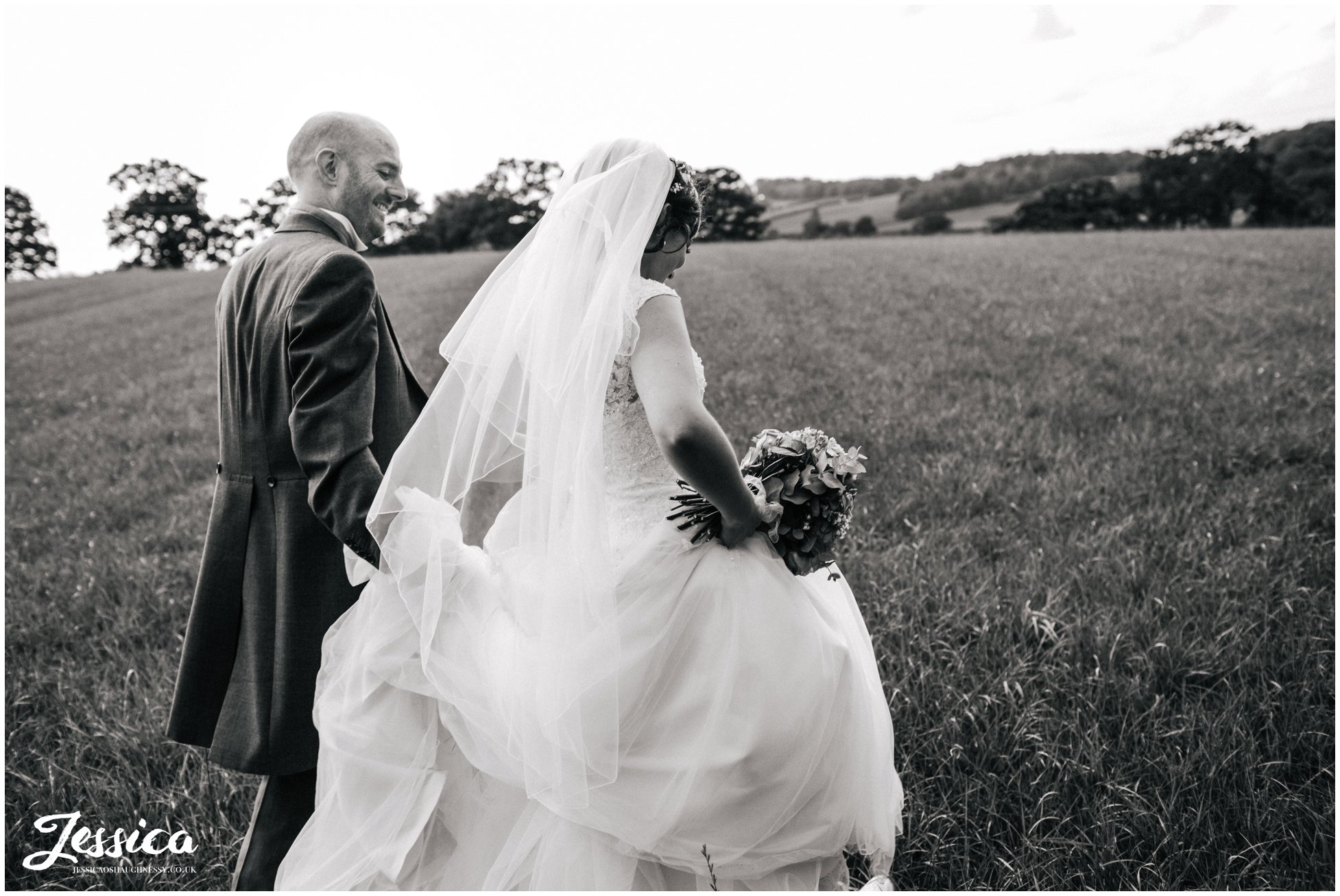 black and white photo of the bride & groom walking through a field at their wedding in cheshire