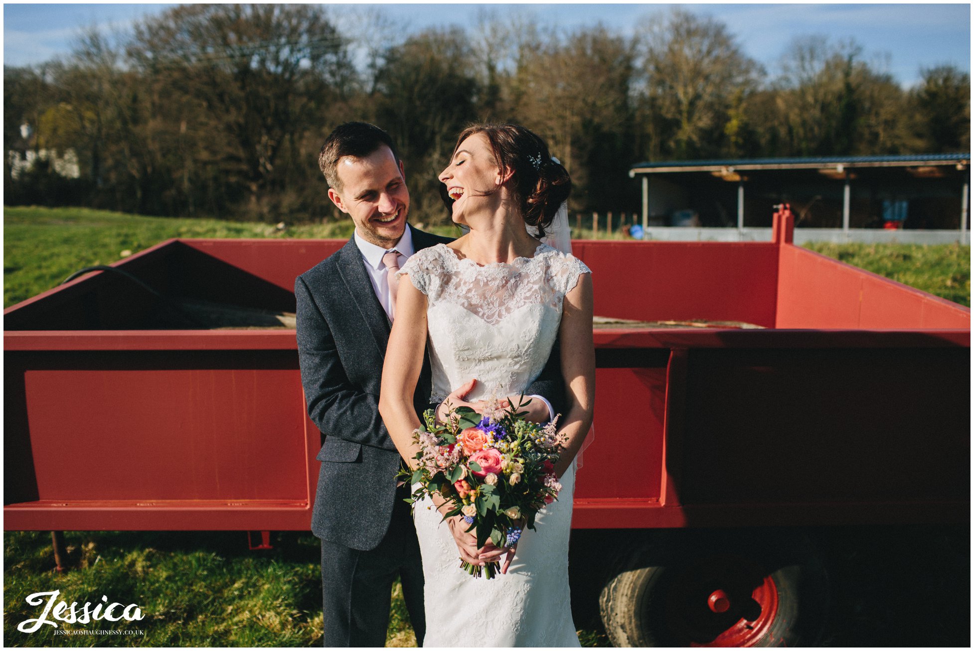 groom embraces bride in front of a red trailer - tower hill barns