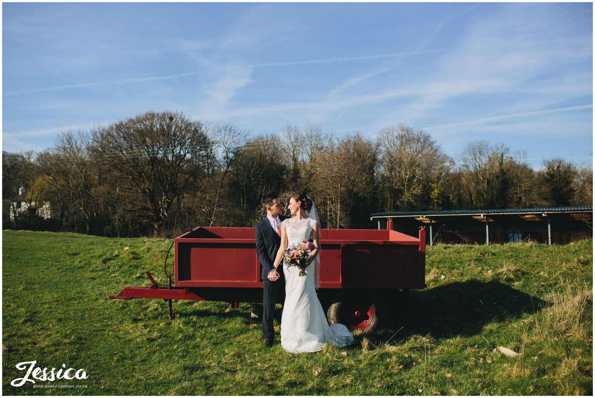 wide shot of newly wed's in front of farming trailer - tower hill barns wedding