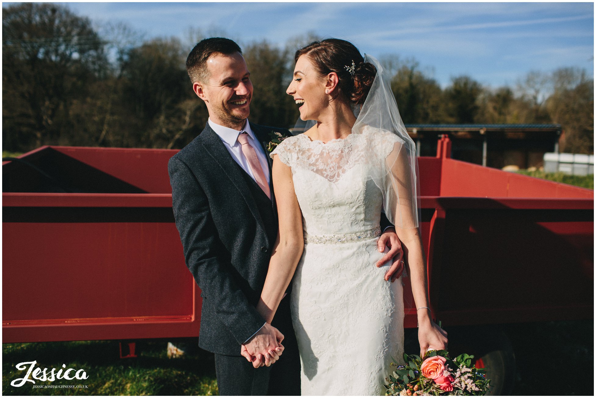 couple laugh in the sun with farm equipment behind them