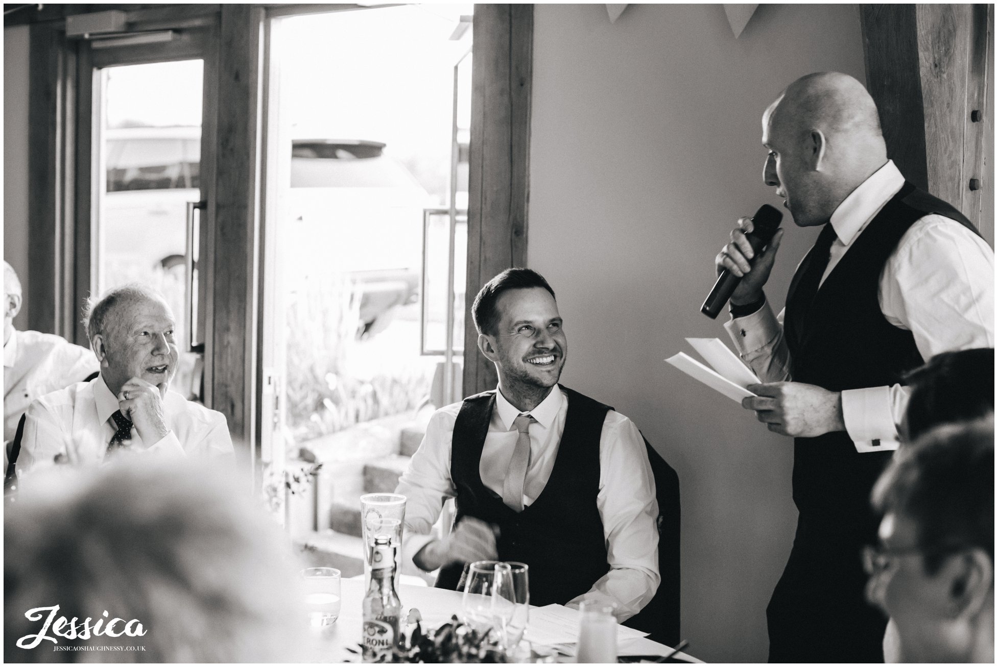 black and white photograph of groom laughing during the speeches in north wales
