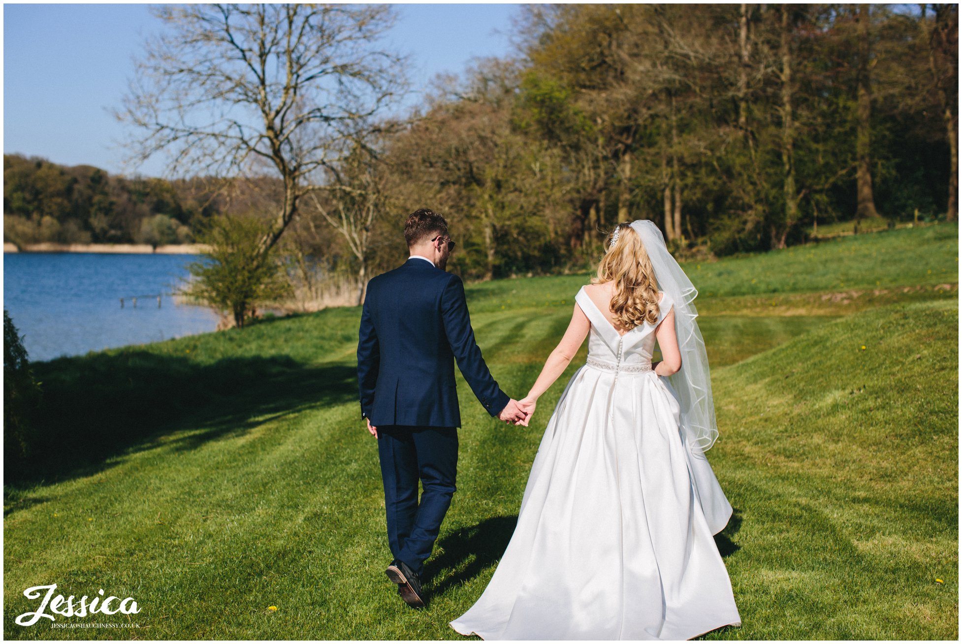 newly wed's hold hands and walk next to the lake