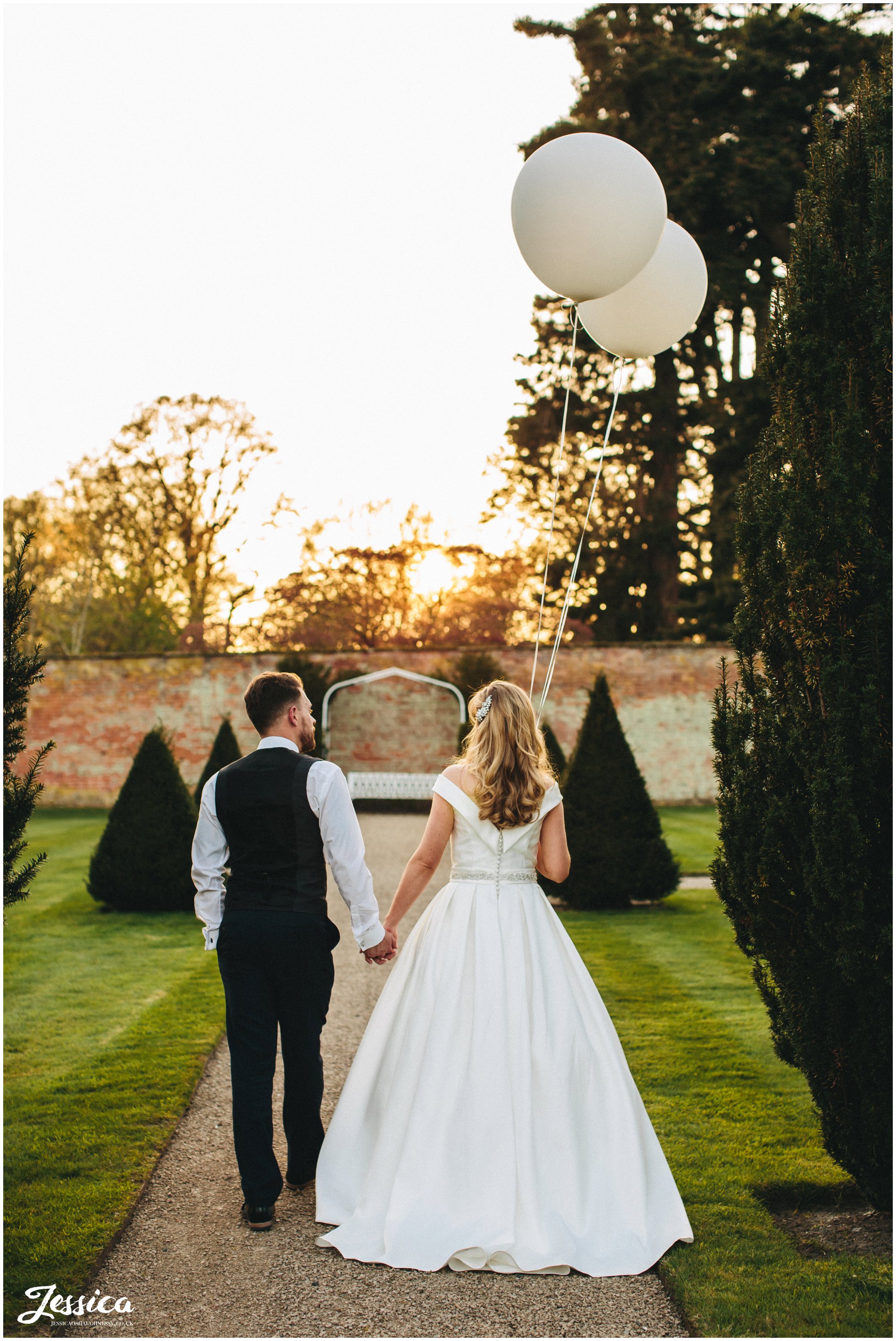 newly wed's walk towards sun set holding big white balloons