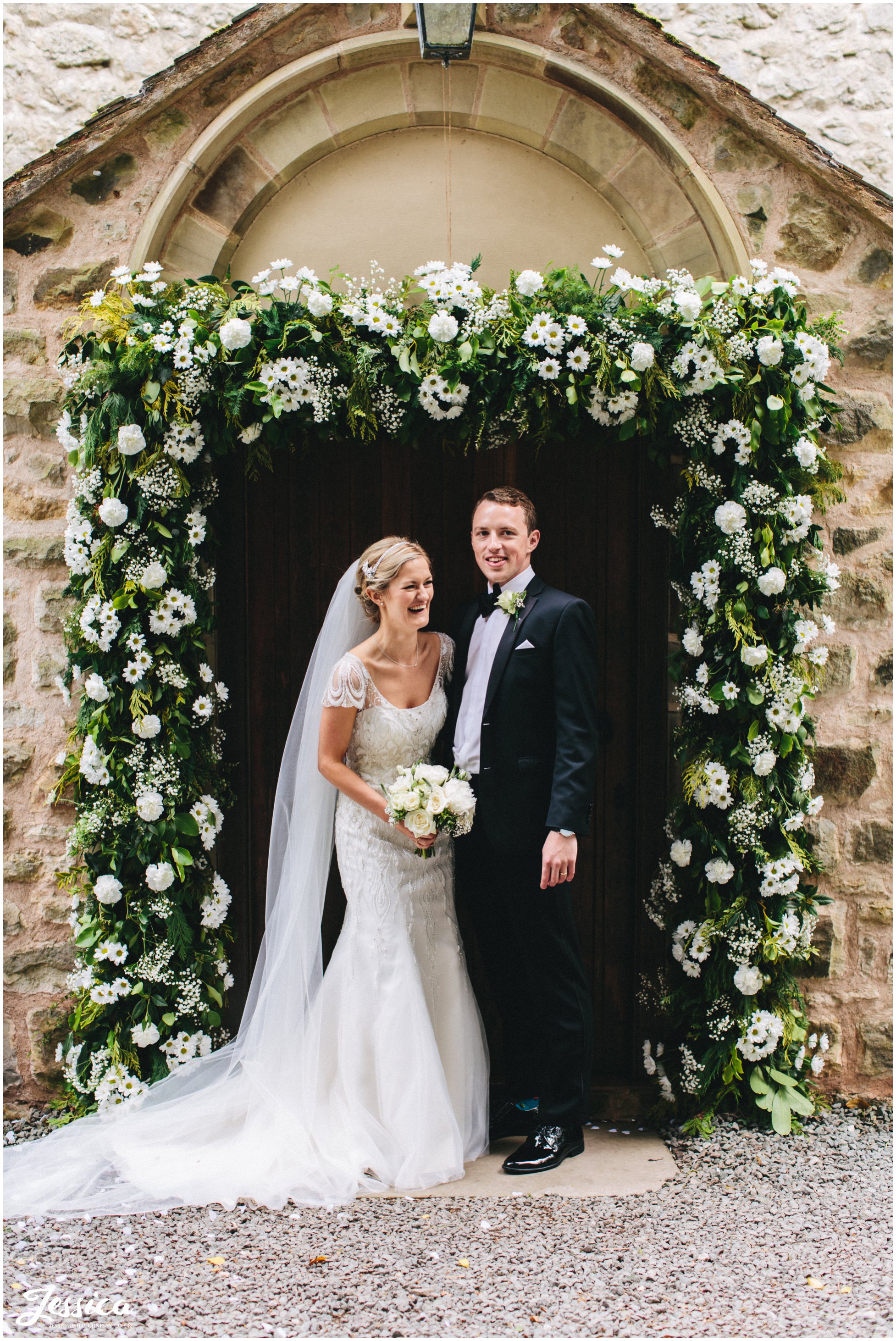 bride & groom stand under their floral arch in Trevor, North Wales