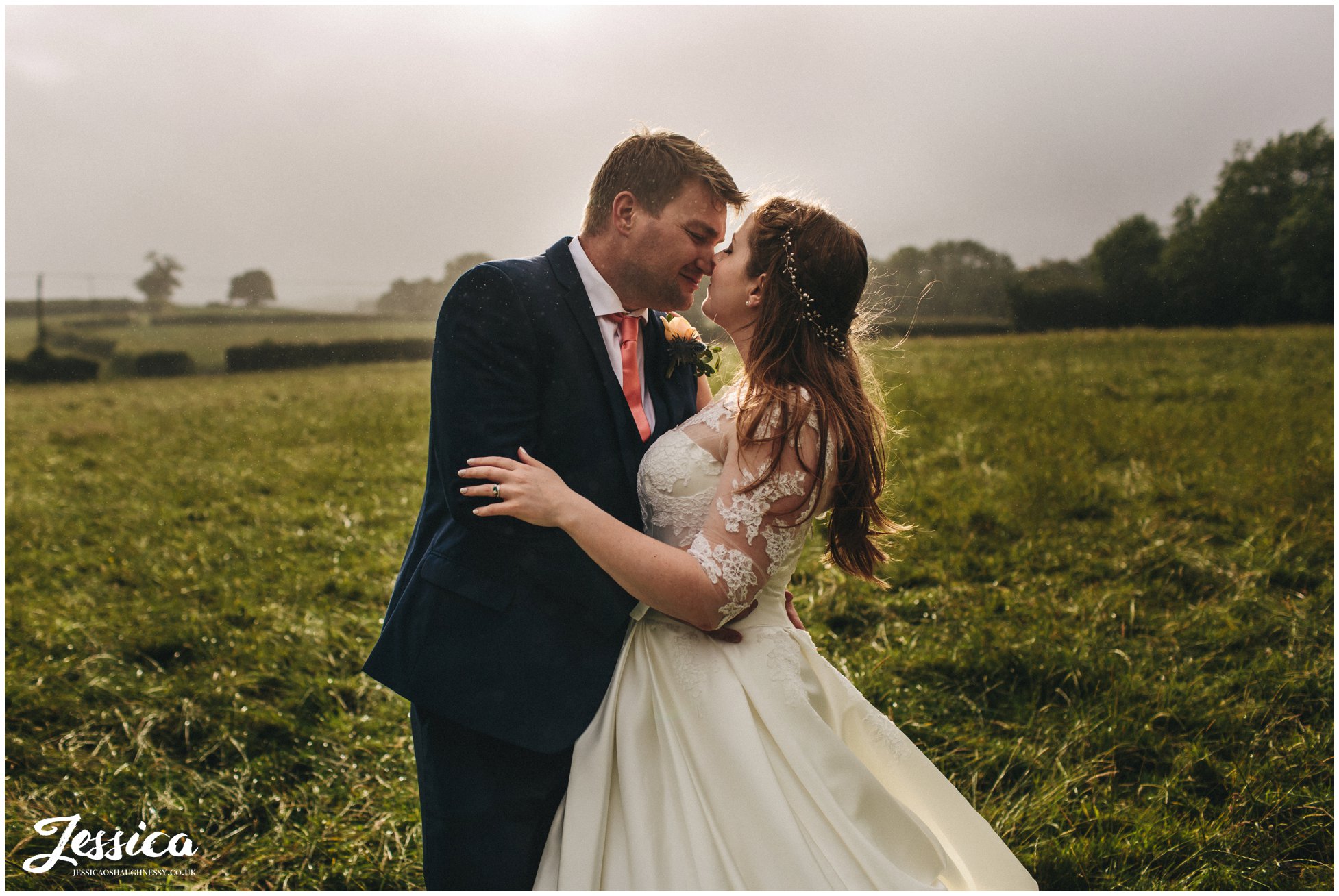 bride & groom kiss in the rain, in the middle of a windy field