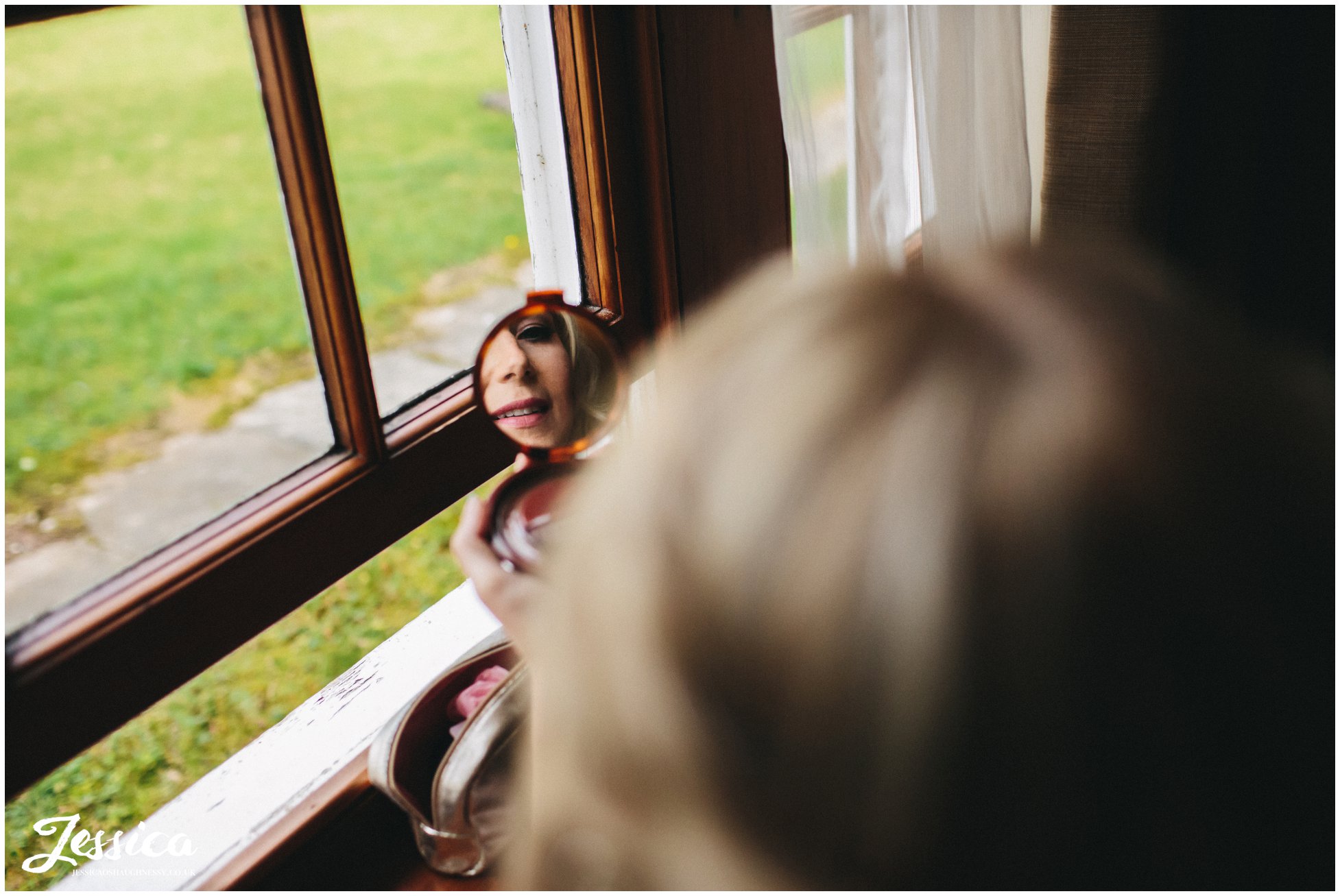 bride checks makeup in mirror - nunsmere hall wedding