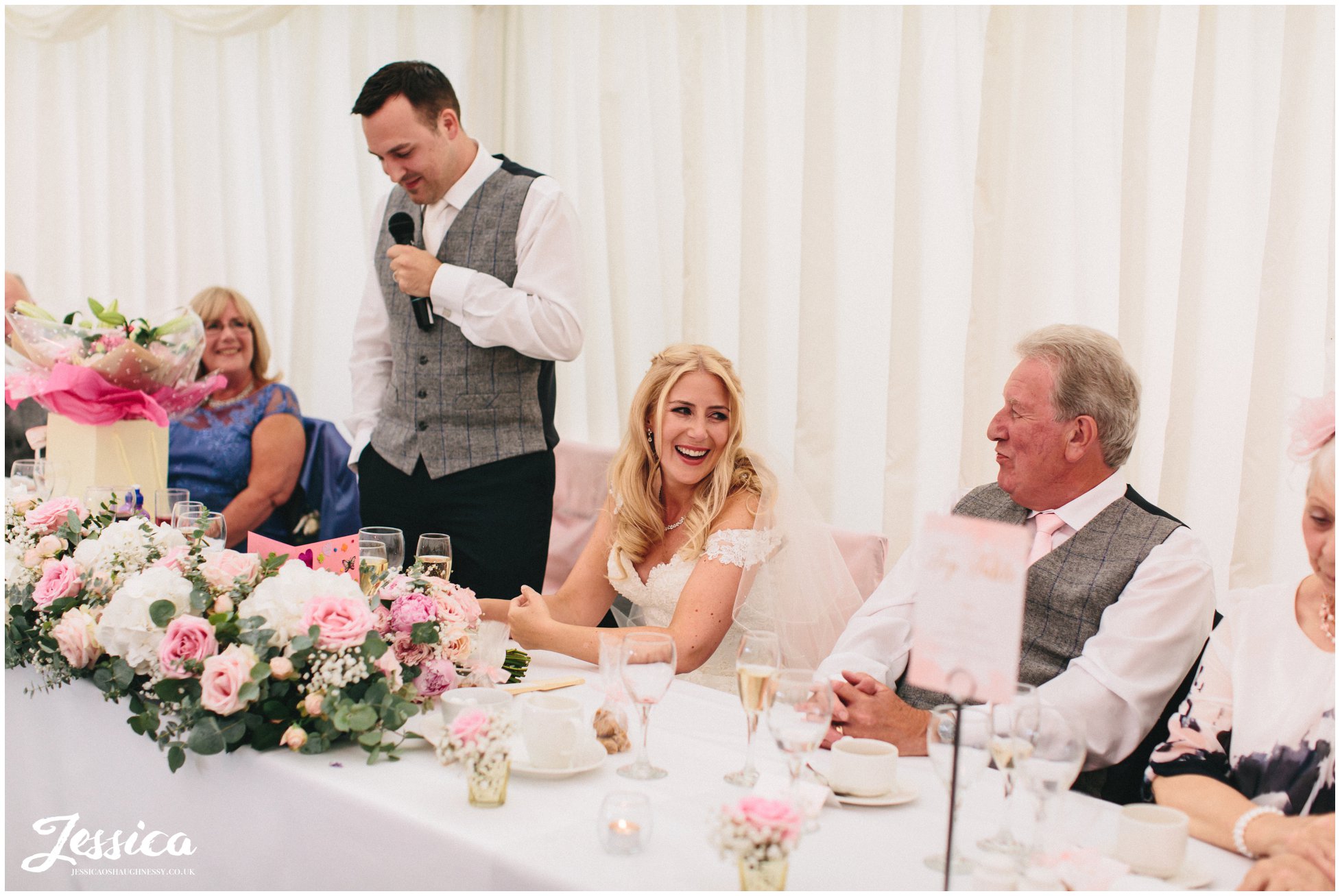 bride enjoying groom's speech at her wedding in nunsmere hall, cheshire