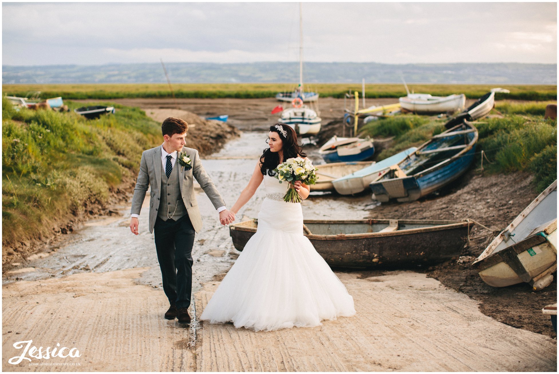 bride & groom walk hand in hand by boats