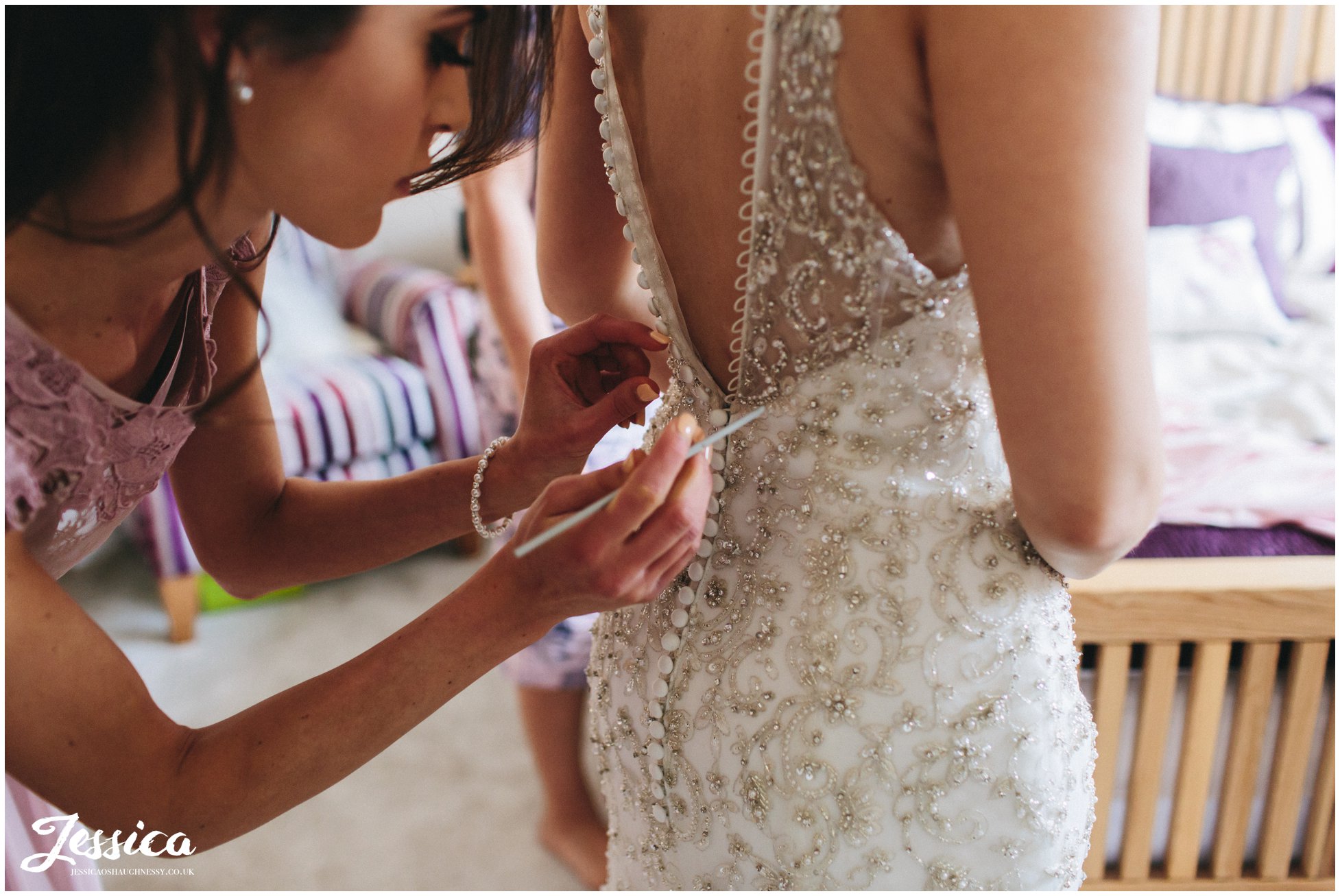 bridesmaid fastens the wedding dress buttons