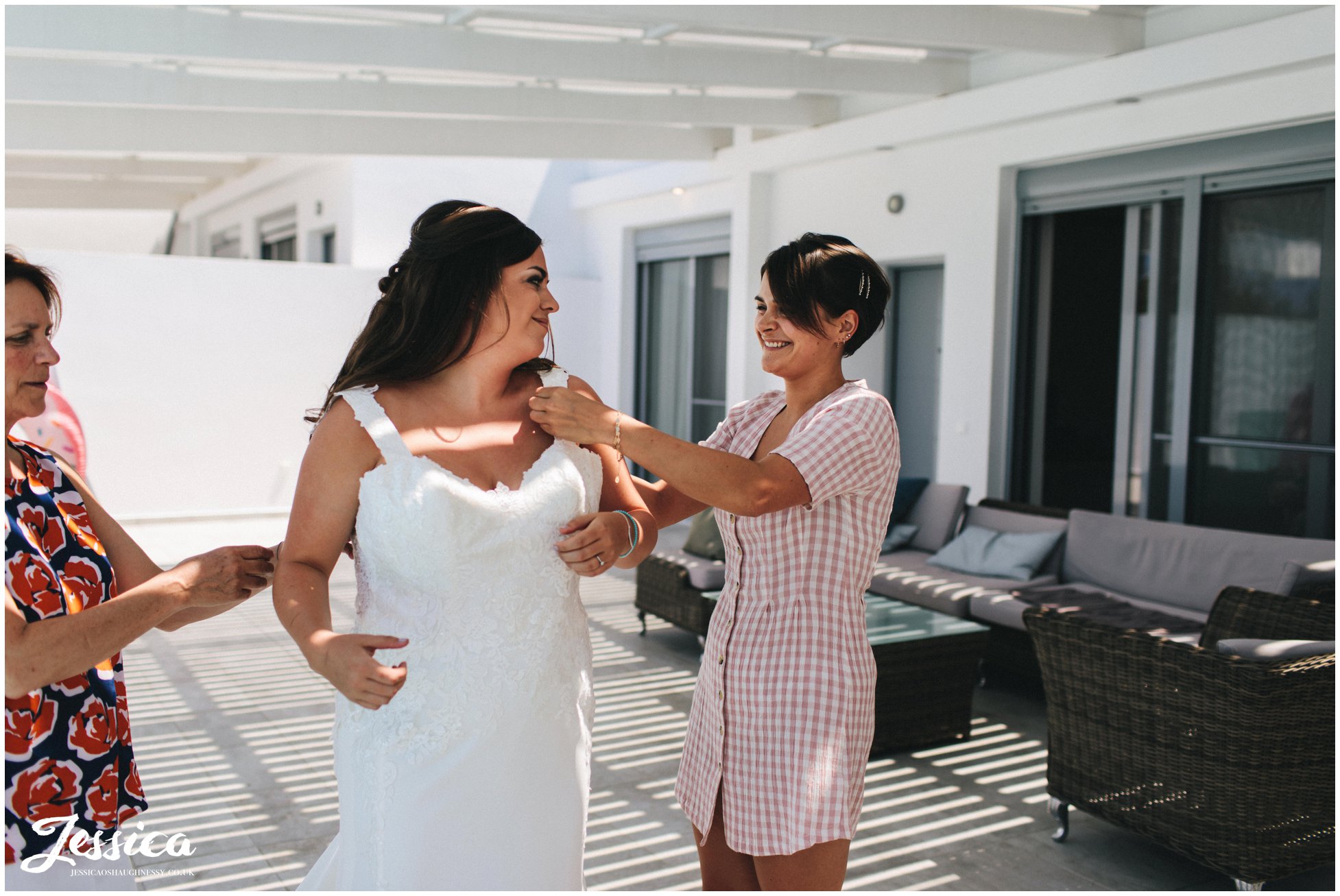 the brides sister and mother help her into her dress