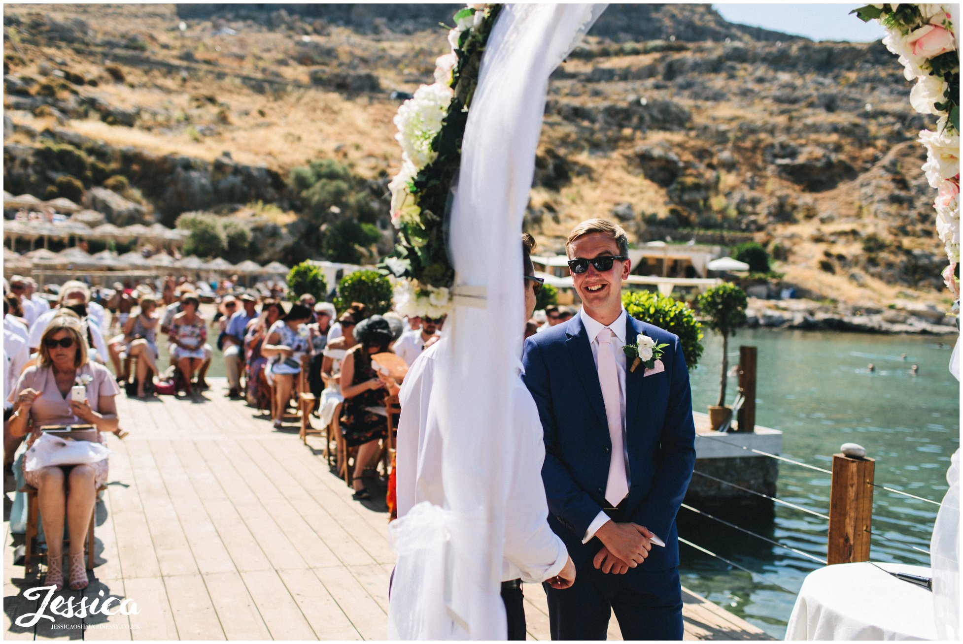 the groom waits for the bride under the flower arch