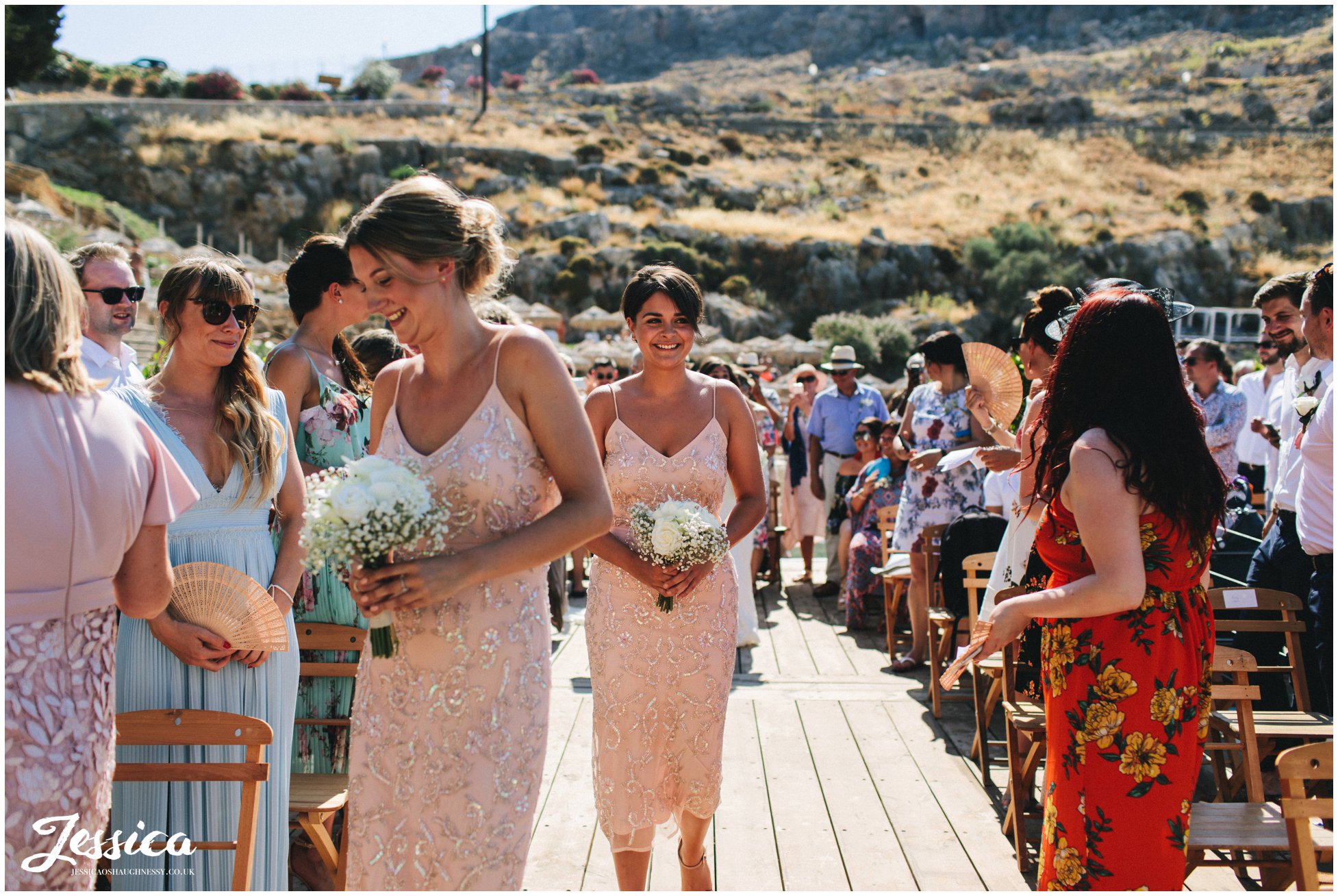 bridesmaids walk down the aisle of the pier at st paul's bay in rhodes