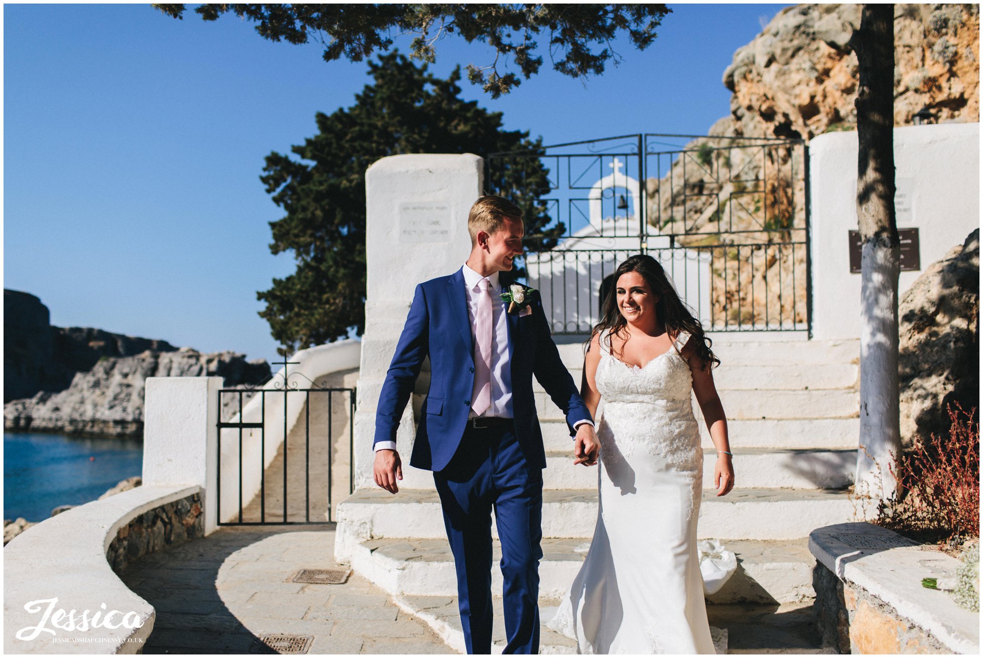 husband and wife walk hand in hand in from of st paul's chapel in rhodes